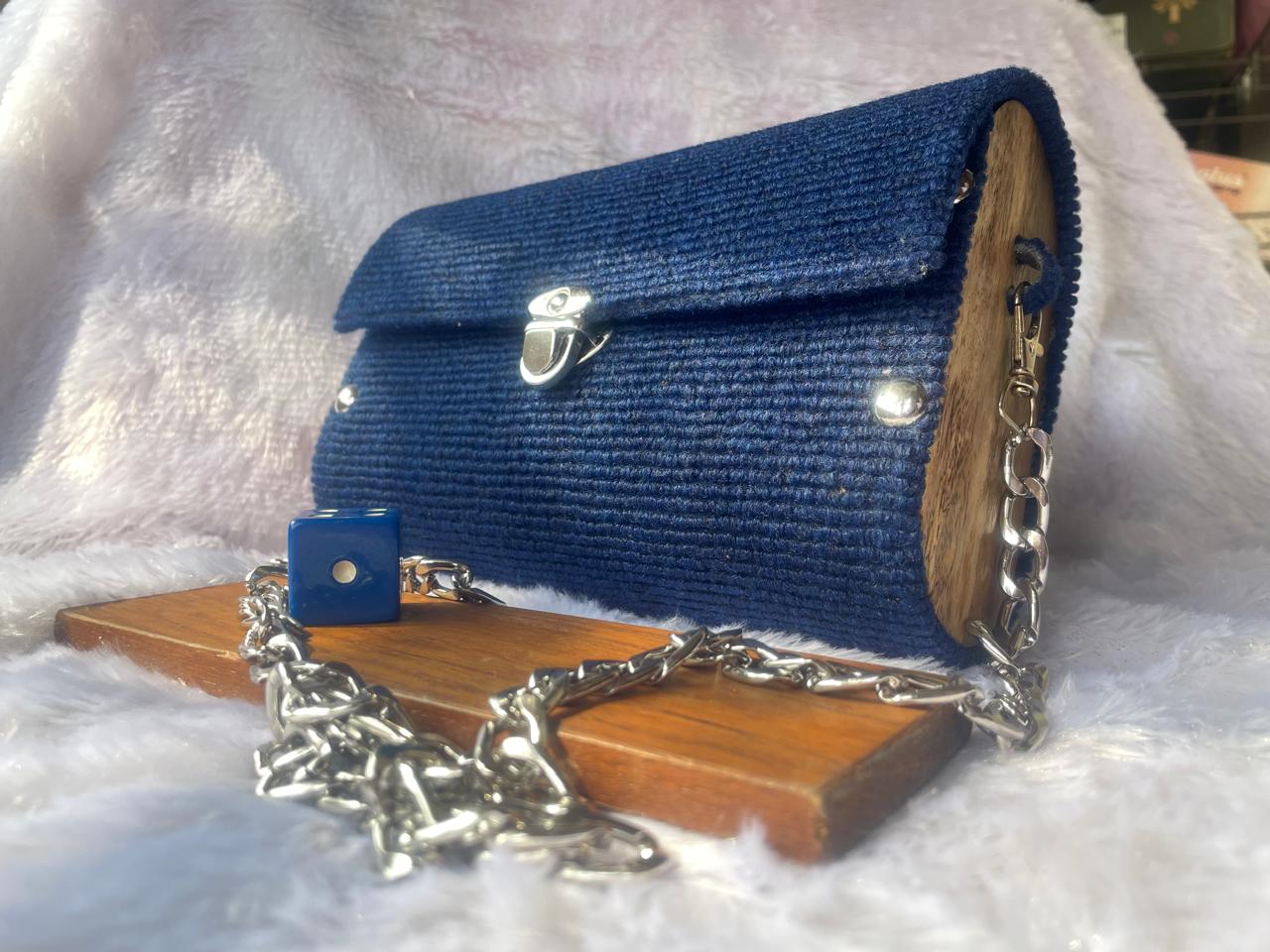 Blue textured clutch purse with a silver clasp, chain strap, and a small decorative element, resting on a wooden surface.