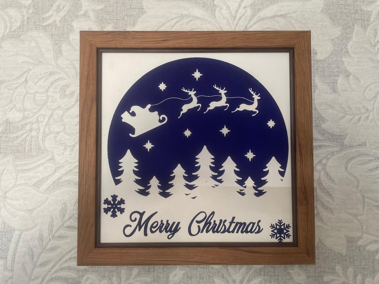 Framed Christmas scene with Santa, reindeer, trees, stars, and snowflakes, with 'Merry Christmas' text at the bottom.