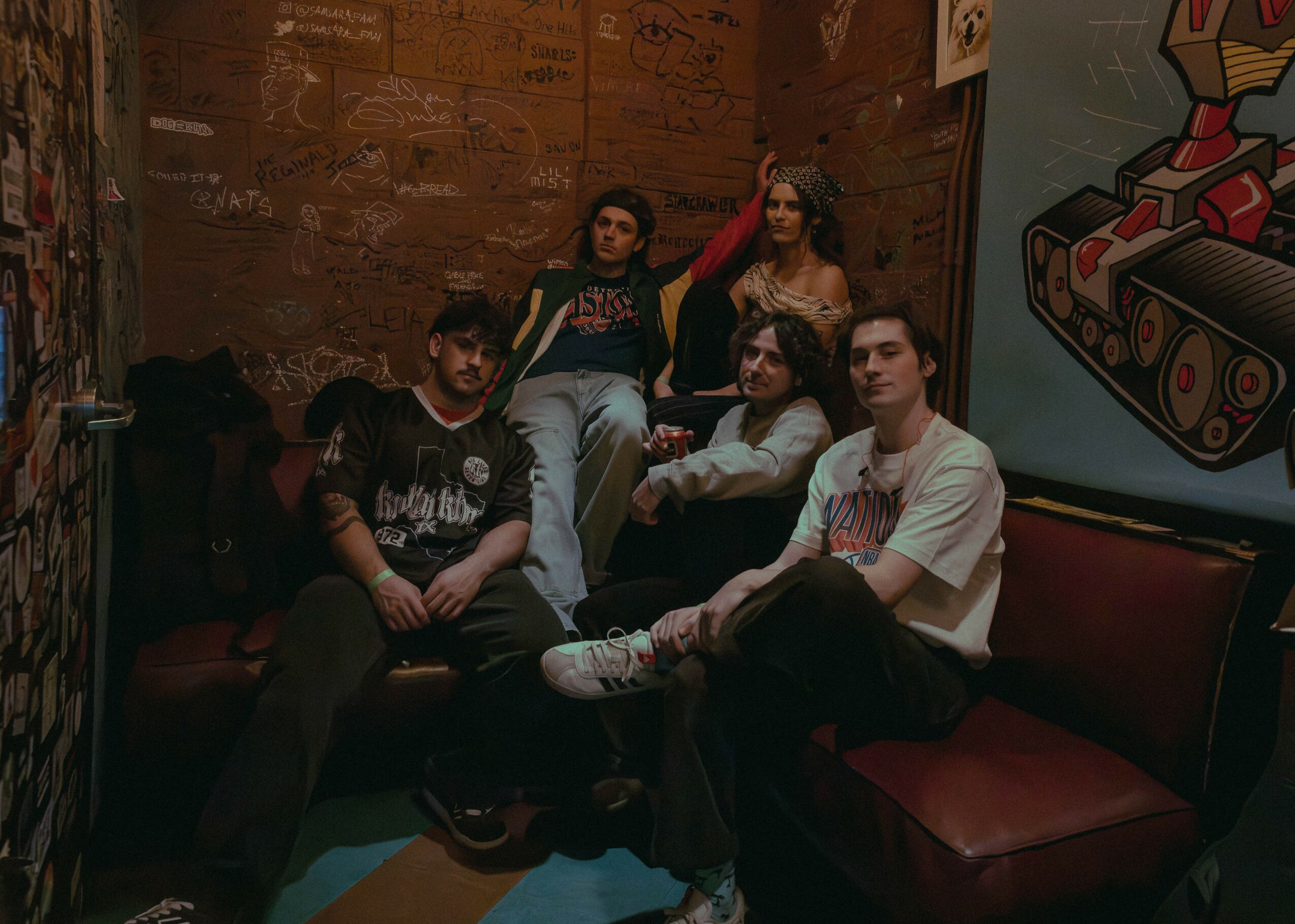 Five people sitting on a red booth in a dimly lit room with brick walls and graffiti art.
