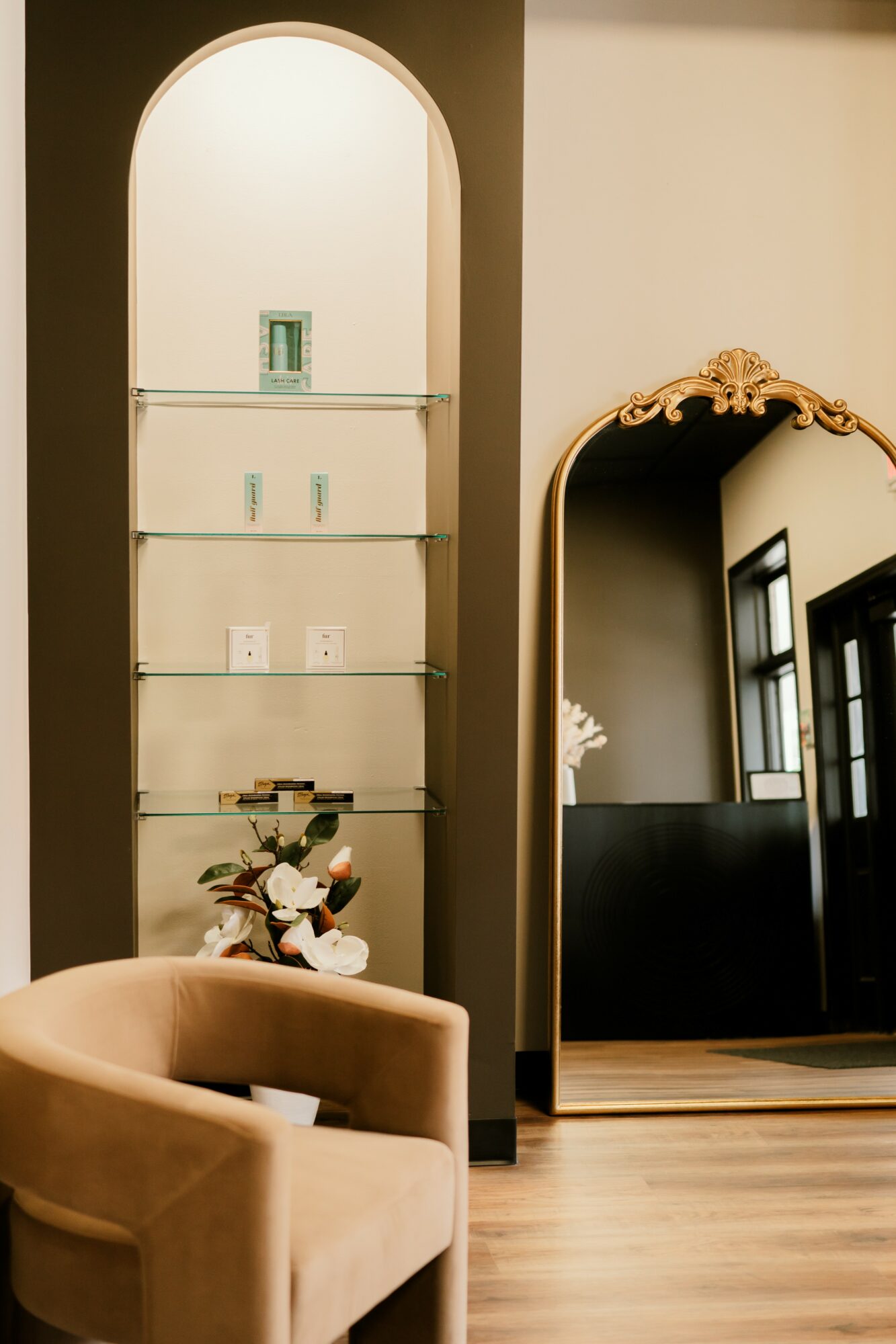 Living room corner with beige armchair, glass display shelf, and a large mirror with ornate frame reflecting windows.