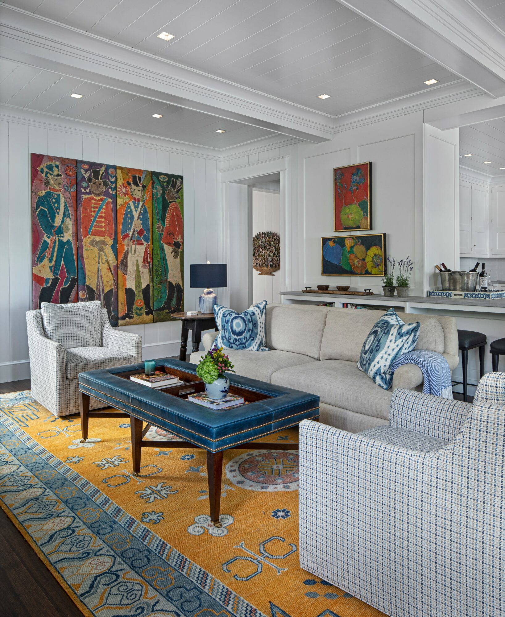 Living room with white walls, colorful artwork, white and blue furniture, and a yellow patterned rug.