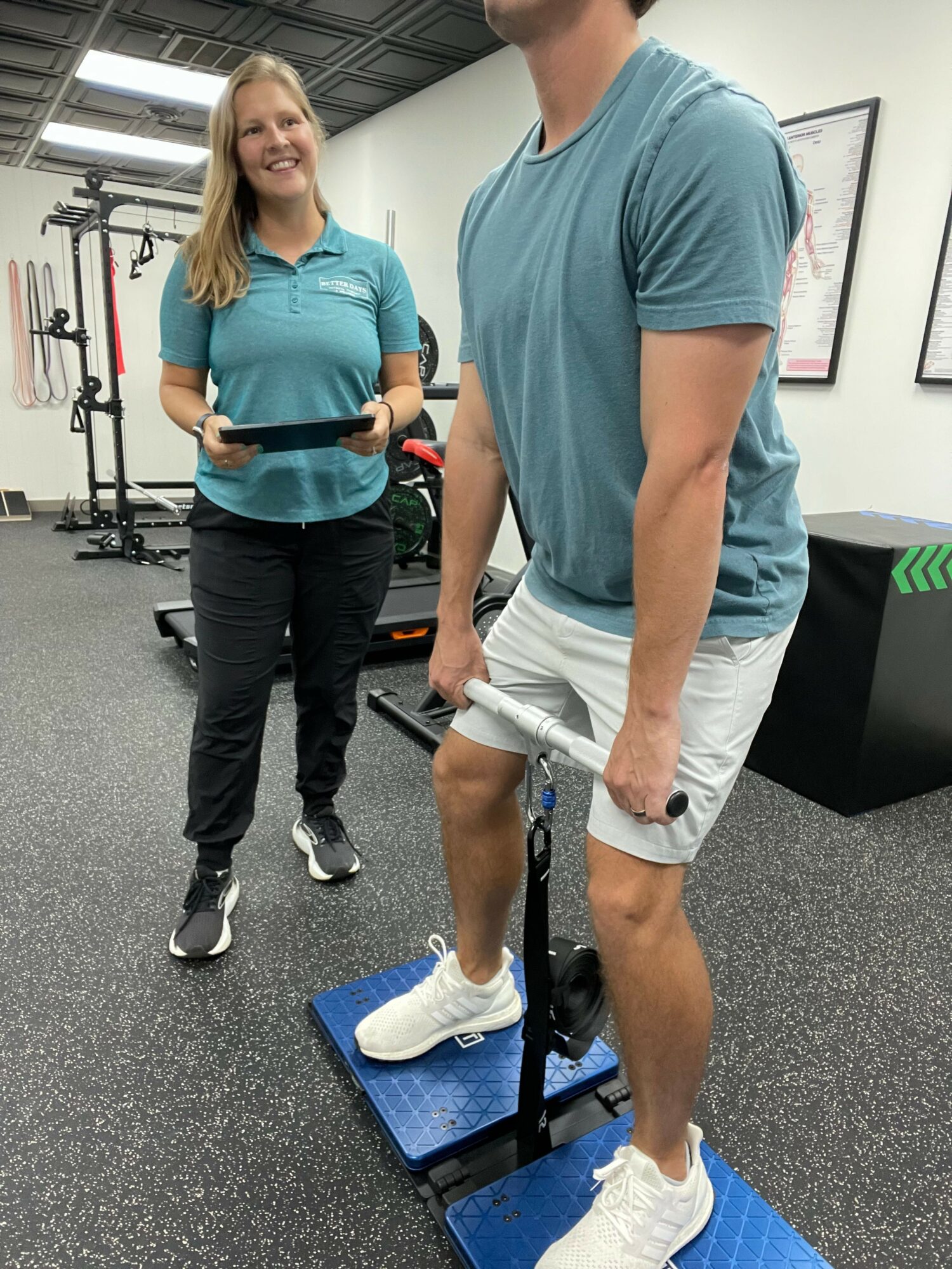 Person in blue shirt standing next to a woman holding a camera, in a gym setting.