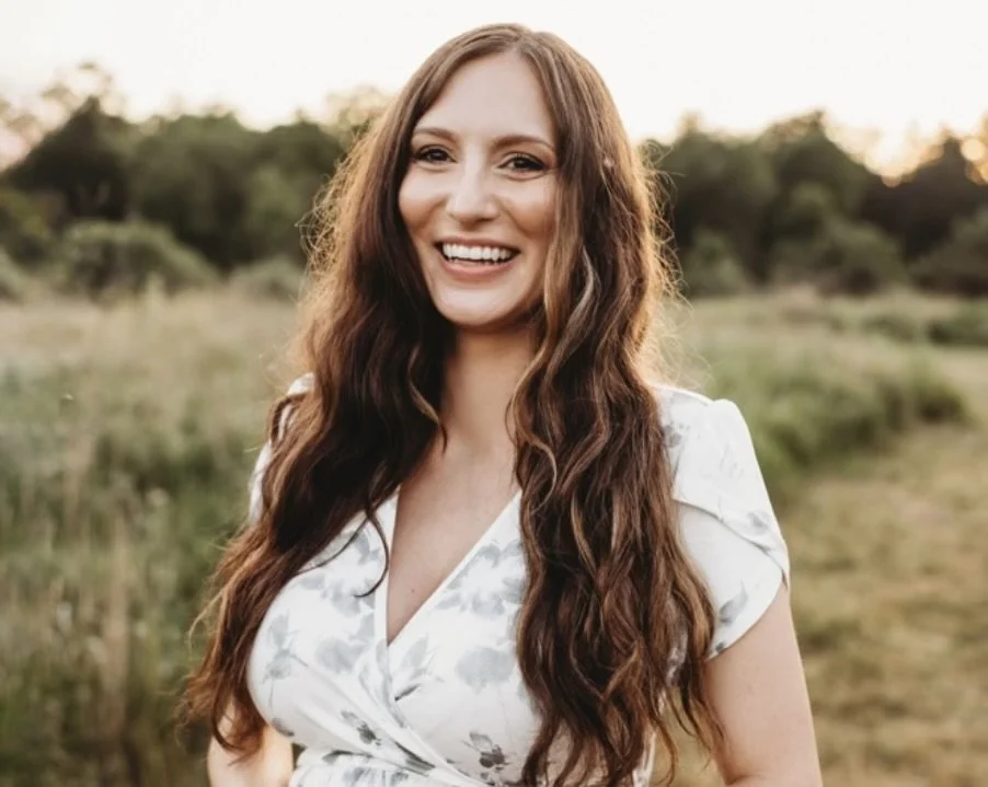 Smiling woman with long wavy hair outdoors in a field during sunset.