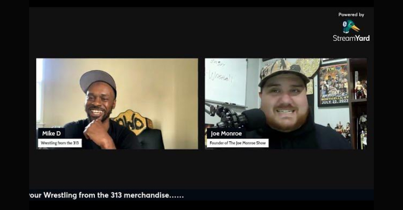 Two men smiling during a virtual interview, one wearing a cap and the other with a hat, with a black background.