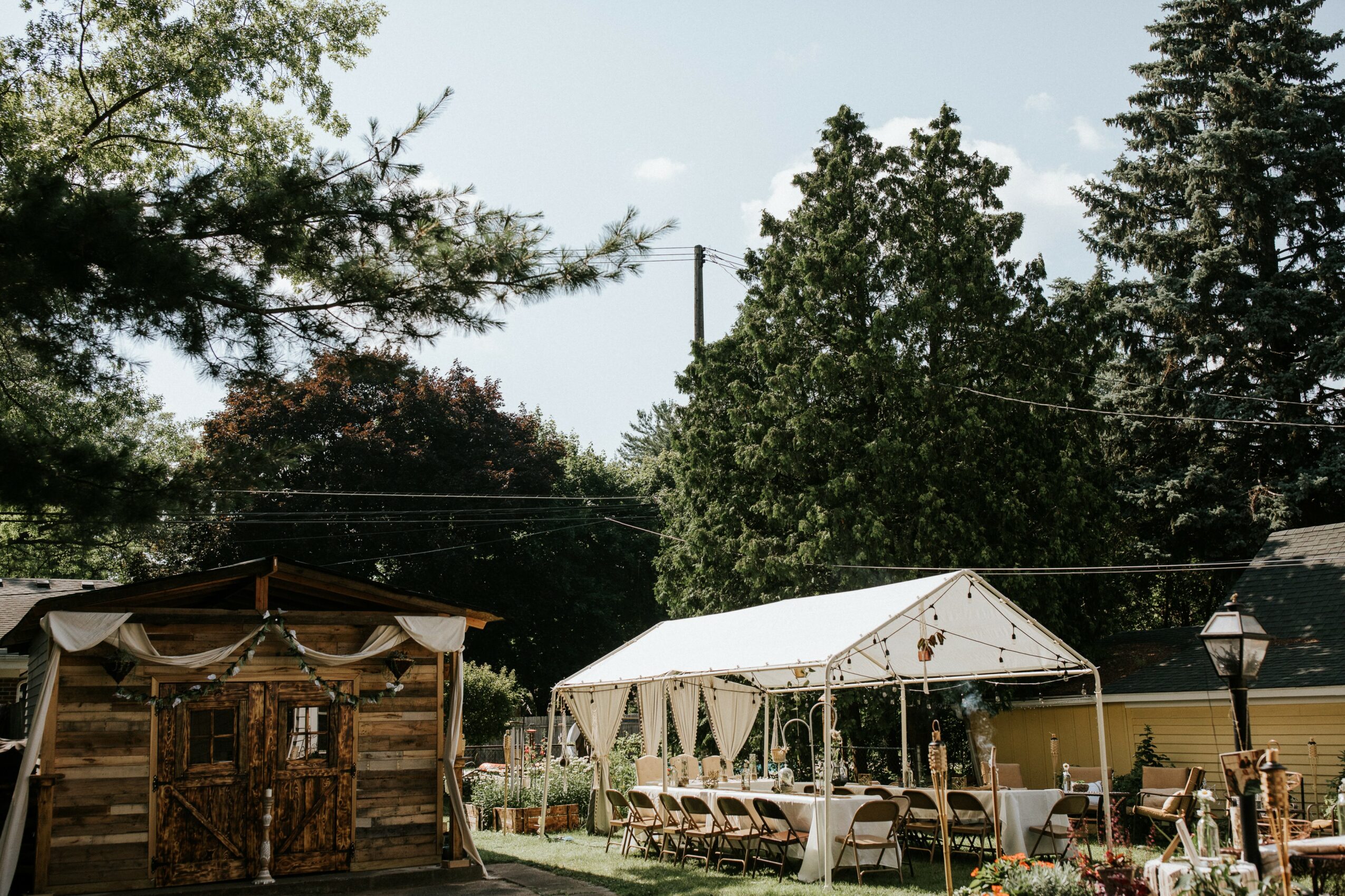Outdoor event setup with tents, tables, and chairs, surrounded by trees and a clear sky.