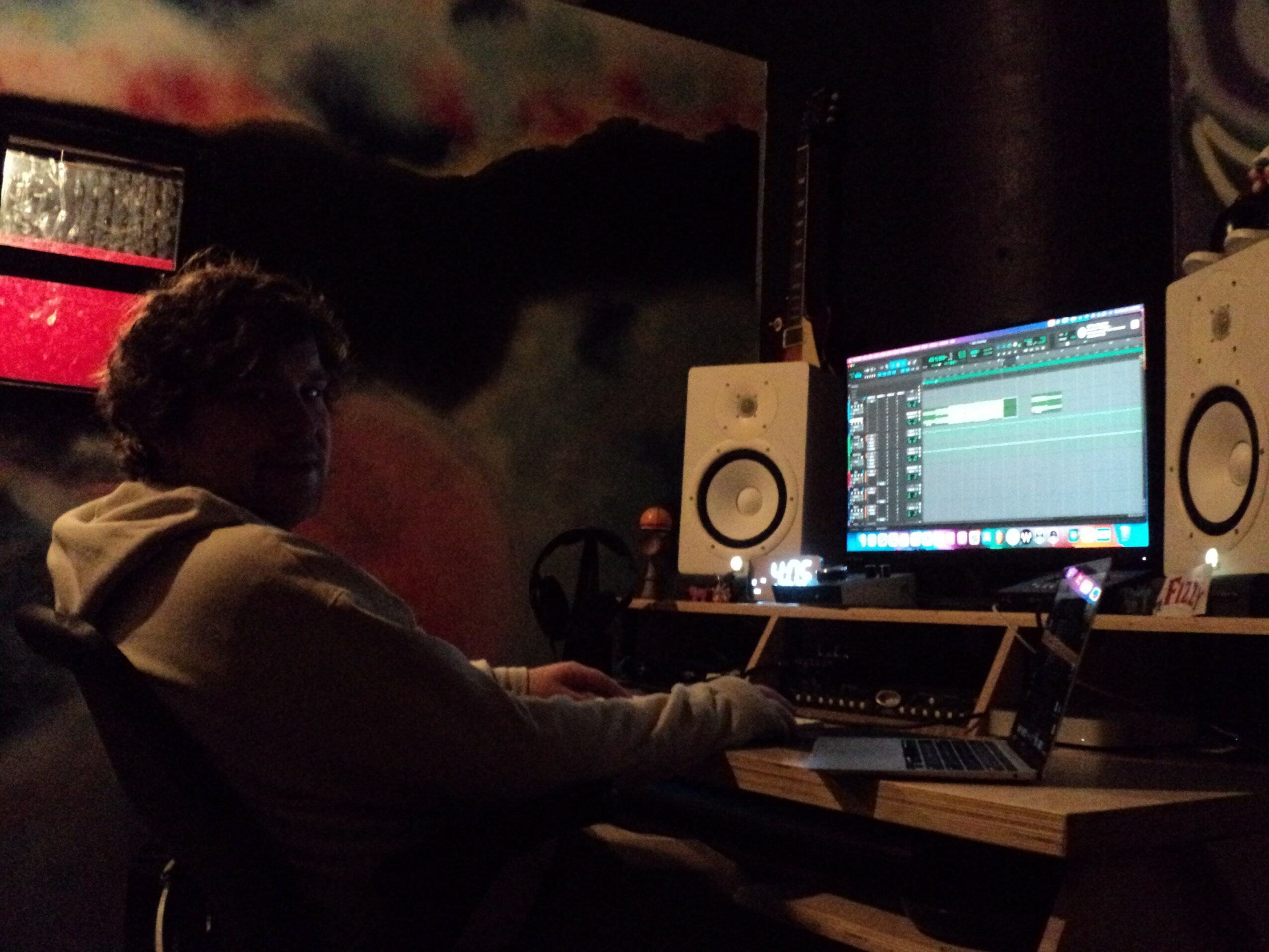 Person working at a computer in a dark room with music production software on screen.