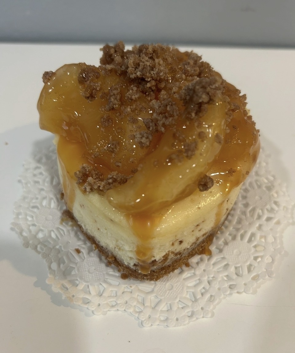 Small dessert with yellow fruit topping, crumbly topping, on a white doily, on a white surface.