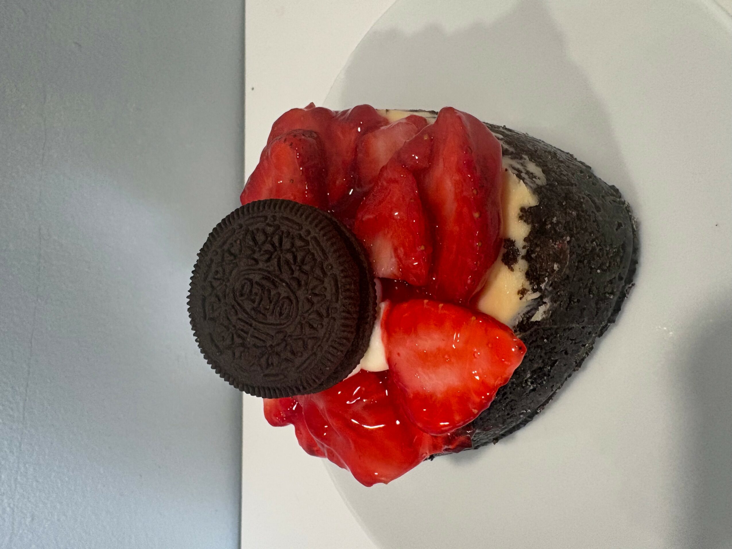 Dessert with strawberries, cream, and a cookie on a white plate.