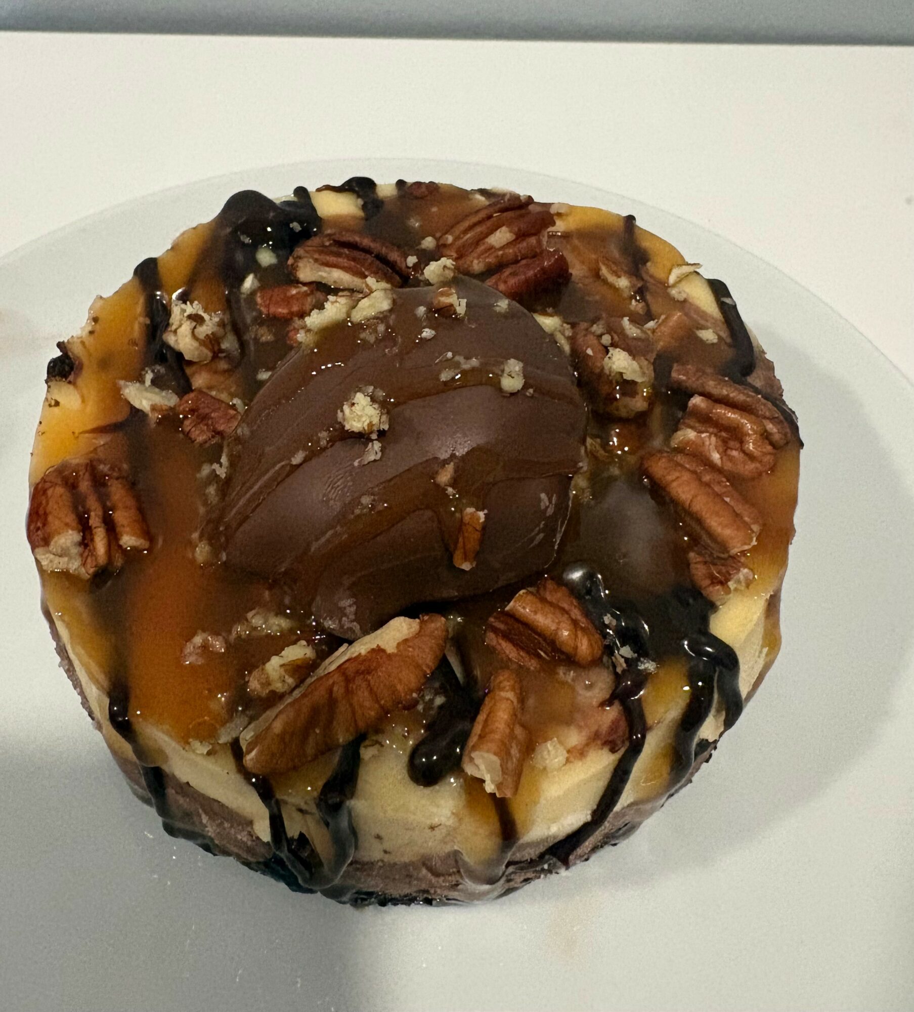 Round dessert with chocolate, caramel, pecans, and a scoop of chocolate ice cream on top, on a white plate.