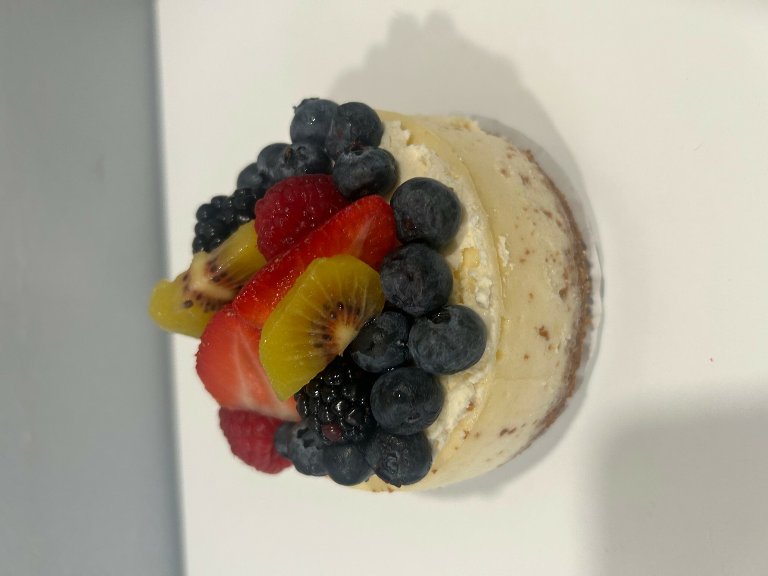 Mini cake topped with mixed berries and sliced kiwi on a white surface.