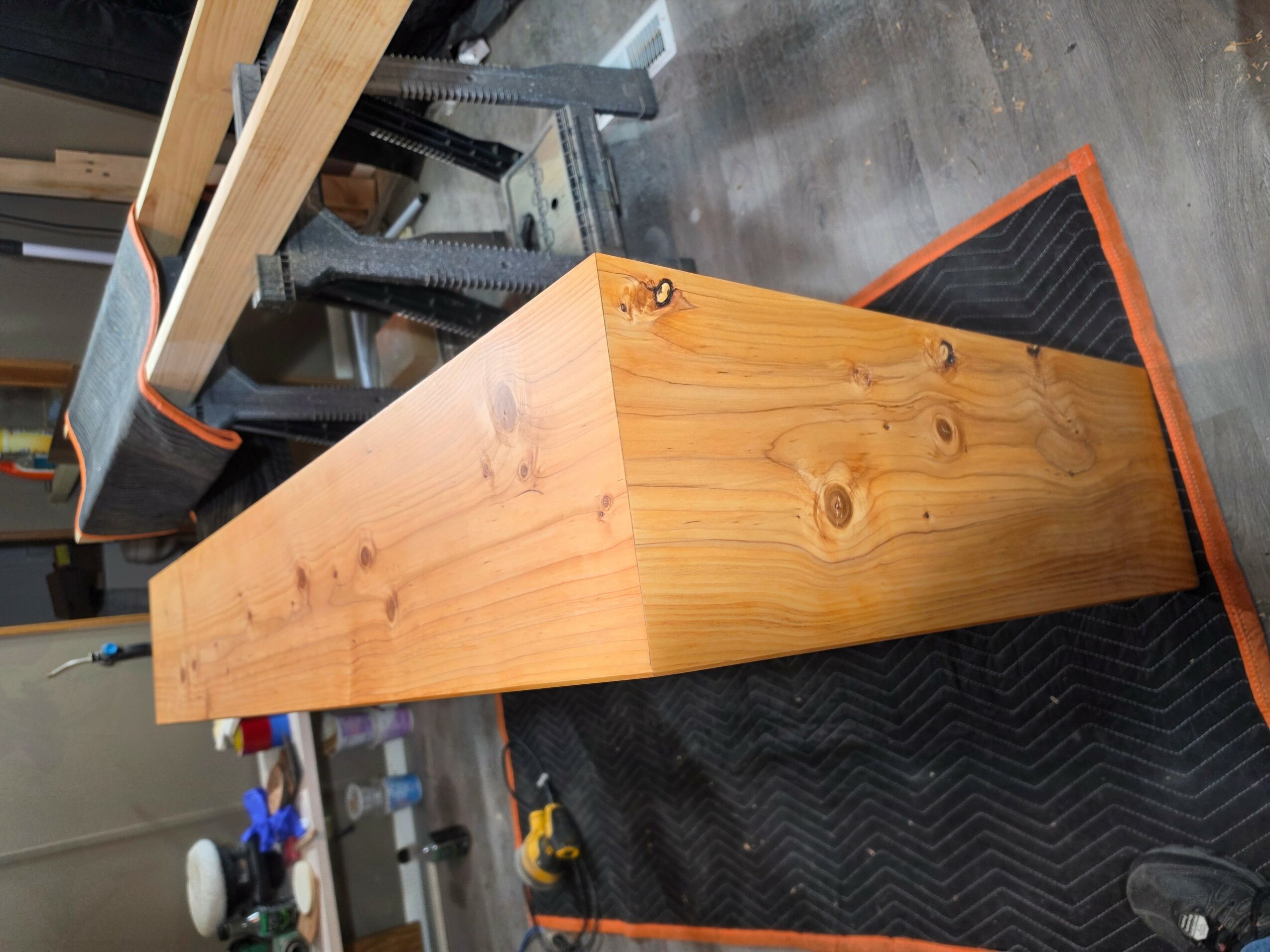 Wooden rectangular block on a black mat in a workshop, with tools and workbench in background.