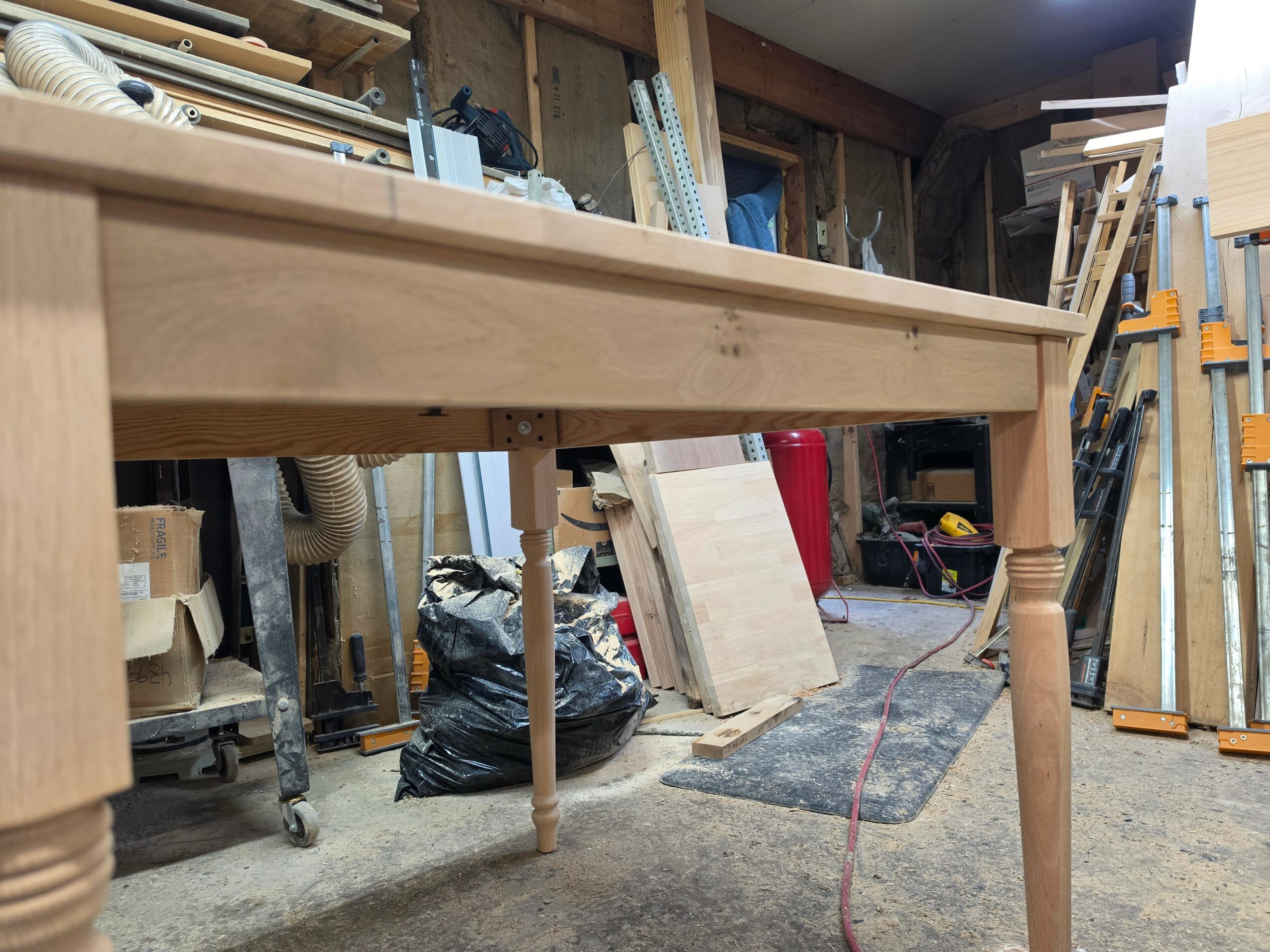 Workshop with wooden furniture, tools, and materials, including a workbench, shelves, and bags of supplies.