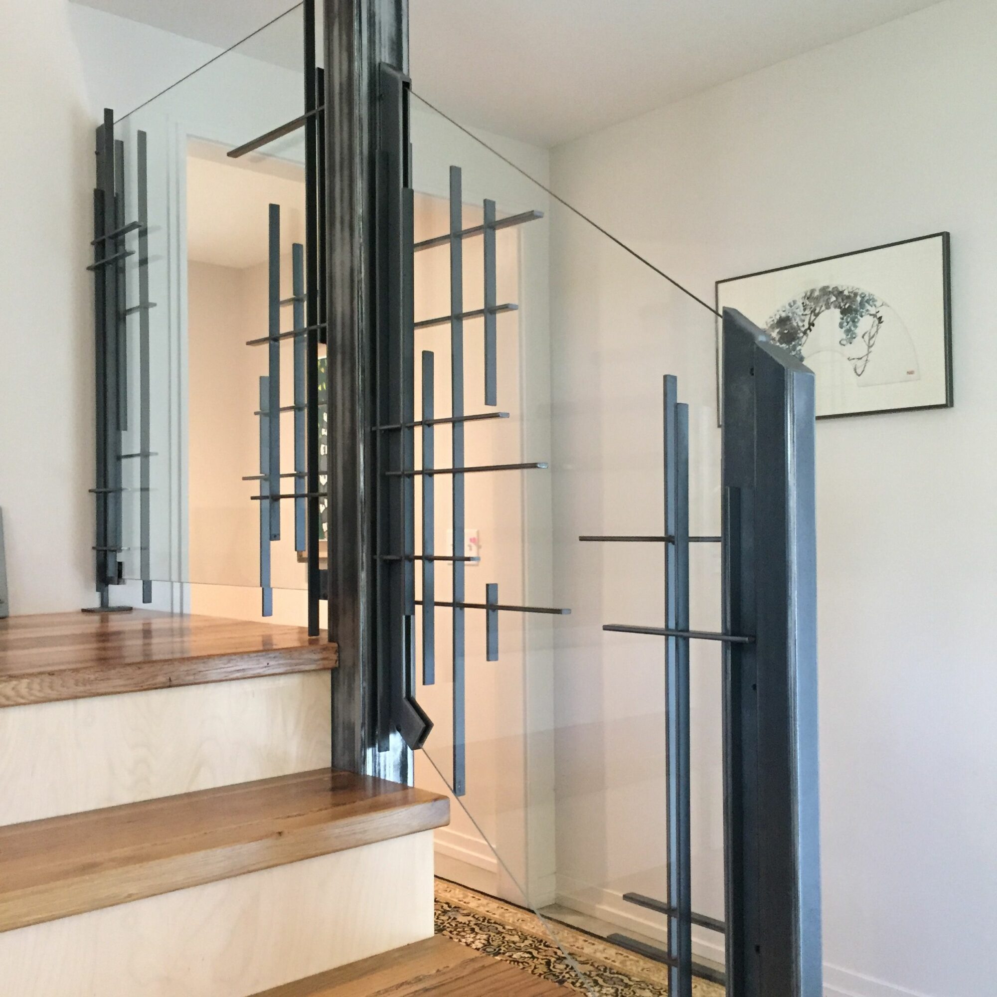 Interior view of a modern space with glass walls, artwork, and wooden stairs, viewed from the side.