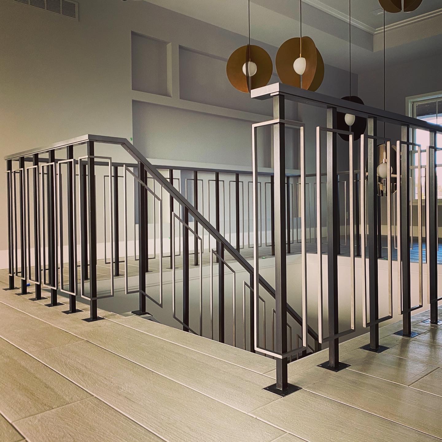 Indoor staircase with black metal railing and light-colored wooden steps, modern decor, pendant lights hanging from ceiling.