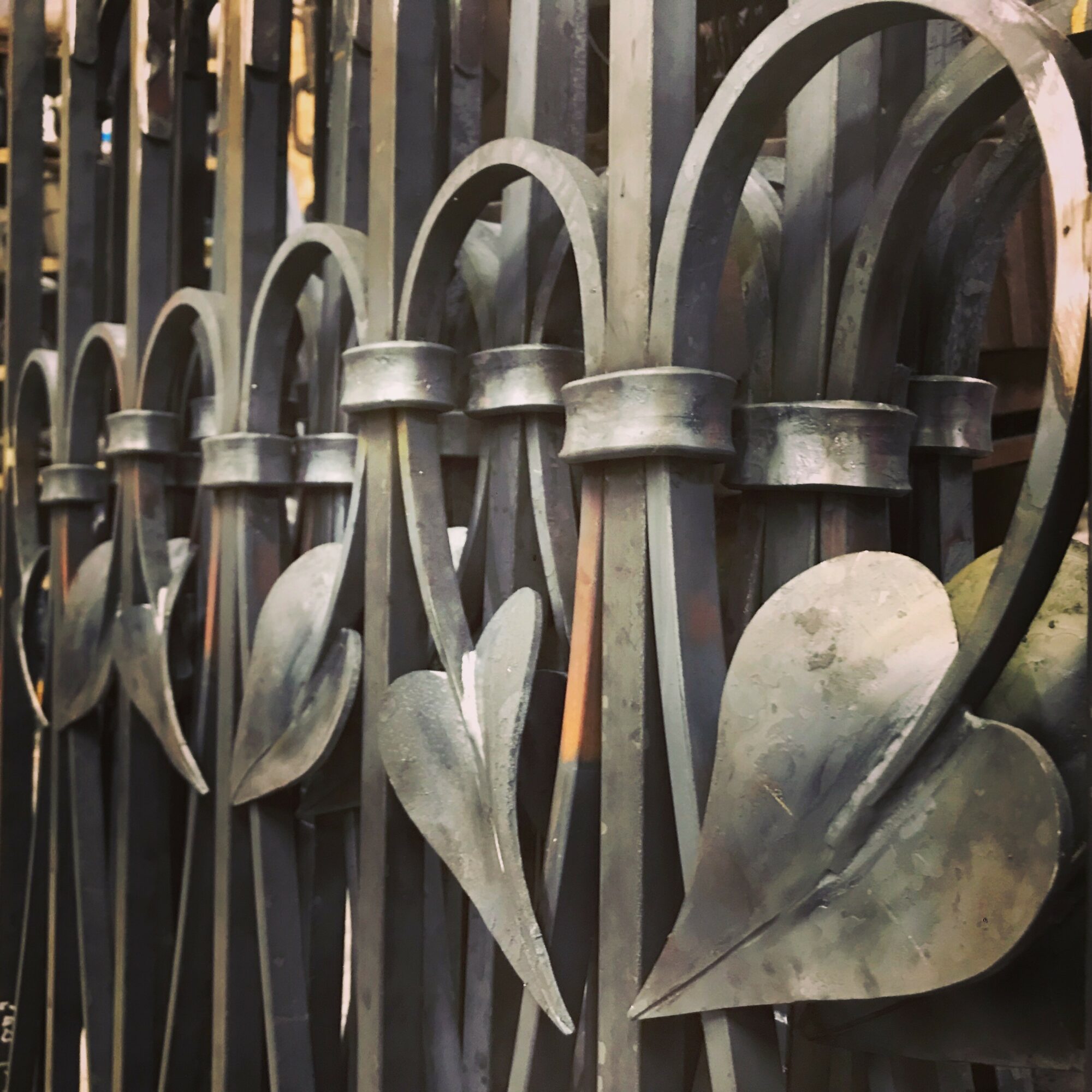 Close-up of a decorative metal fence with heart-shaped and leaf-shaped elements, showing a weathered surface.