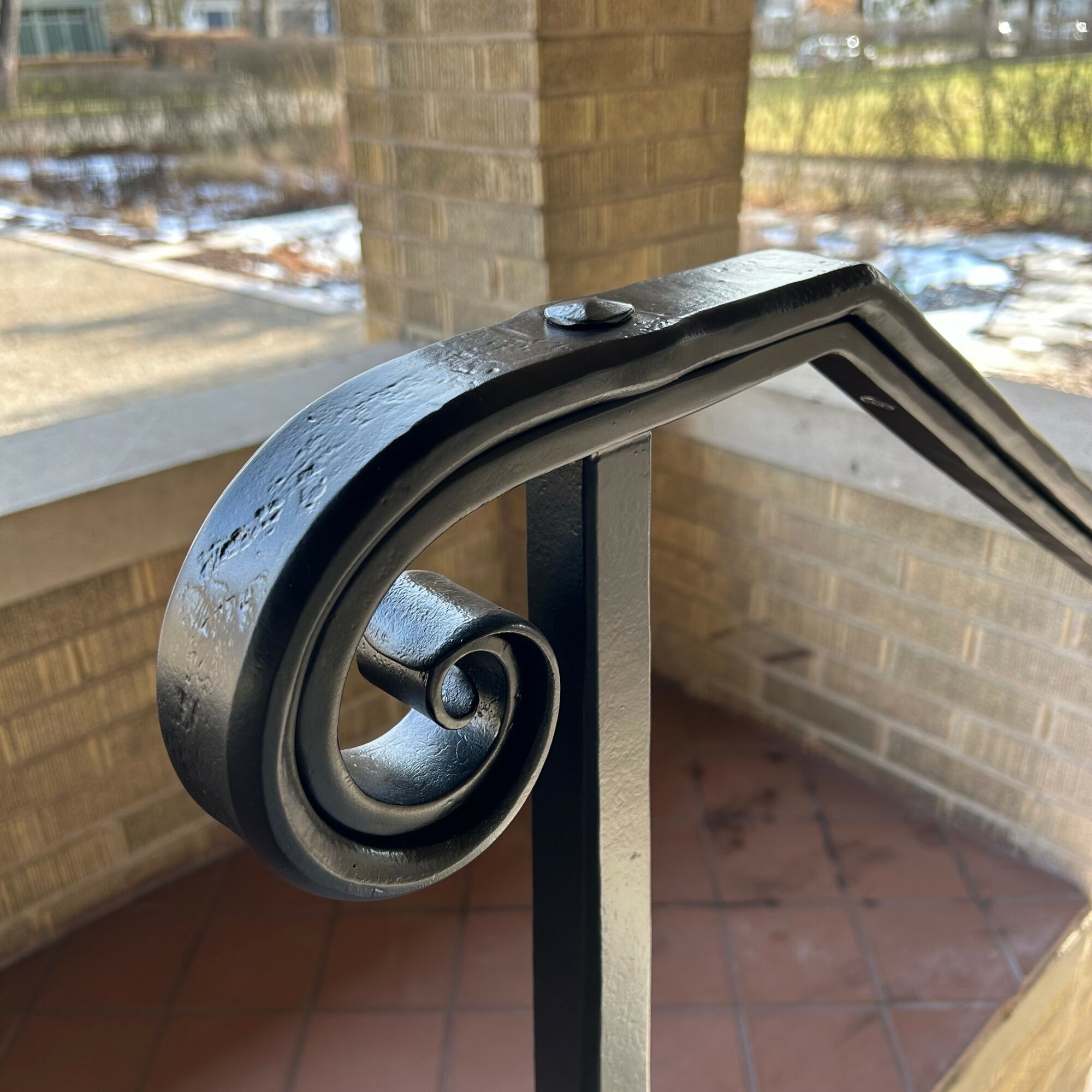 Close-up of a black metal handrail with a decorative spiral end, attached to a brick wall outside.