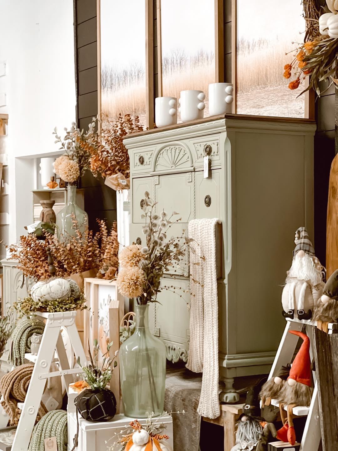 Decorative cabinet with flowers, candles, and ornaments in a cozy interior setting, surrounded by plants and decorative items.