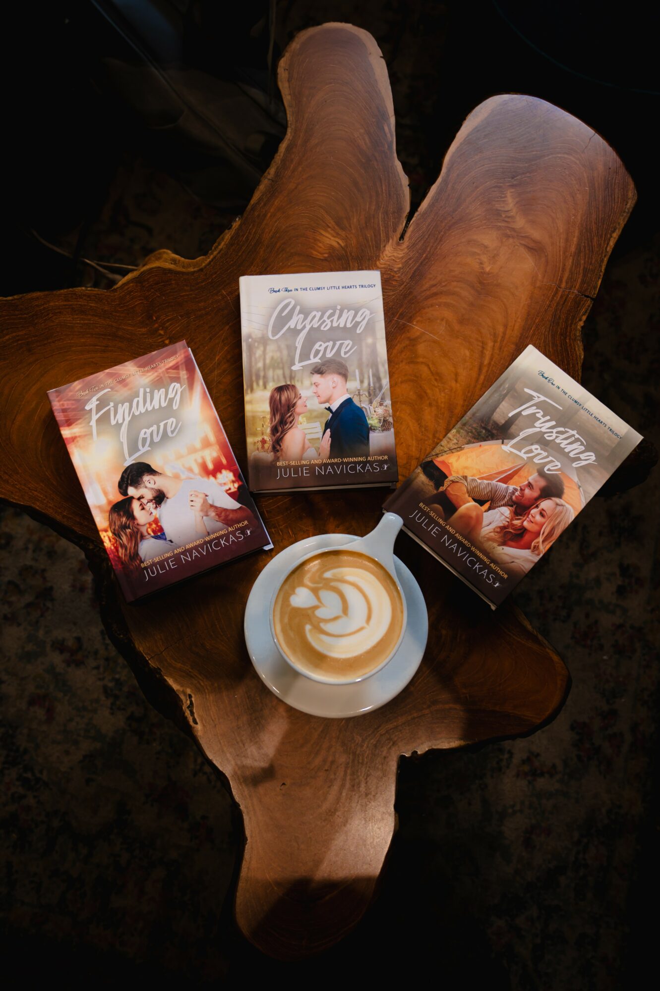 Three books with romantic covers and a cup of coffee on a wooden table, viewed from above.