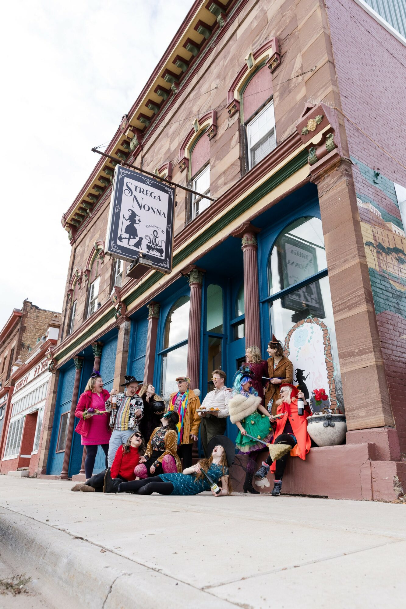Group of people gathered outside a building with colorful columns and a sign that reads 'Saddle Up Now.'