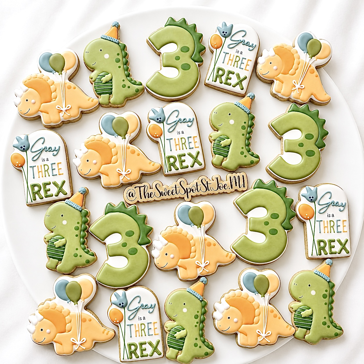 Decorative cookies with dinosaur, number 3, and balloon designs for a birthday celebration, arranged on a white surface.