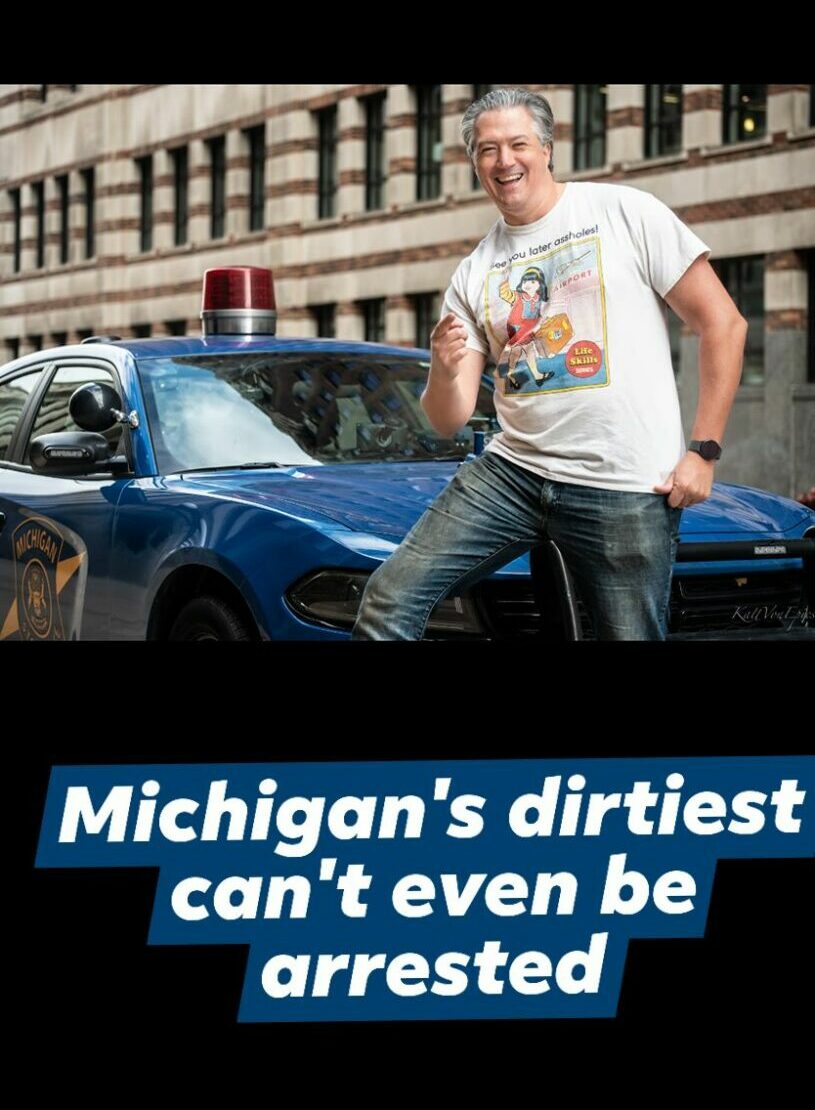 Person standing next to a police car on city street, smiling, with buildings in background.