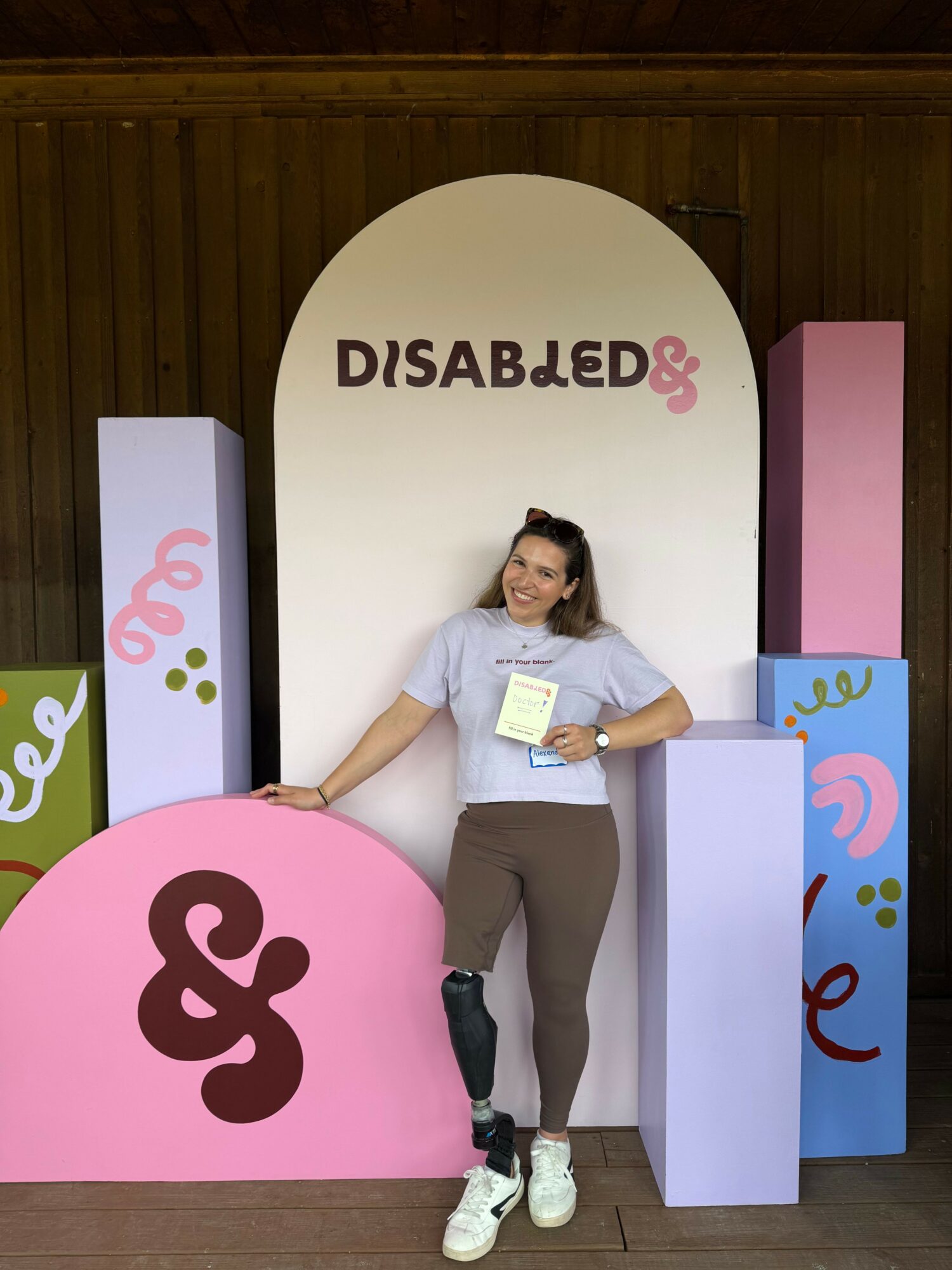 Woman standing next to colorful display with text 'DISABLED' and decorative shapes, in an indoor setting.