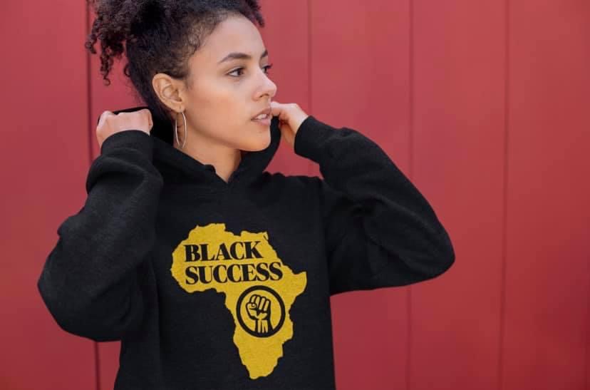 Young woman with curly hair wearing a black hoodie with a yellow Africa map and text, standing against a red background.