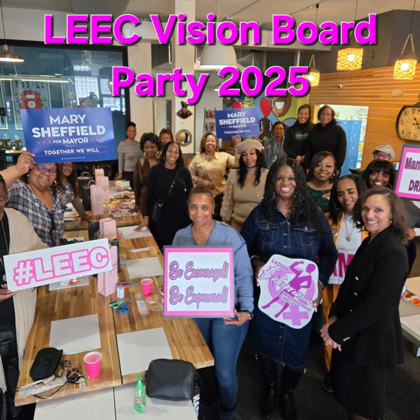 Group of people gathered indoors for a celebration, with signs and decorations, celebrating LEEC Vision Board Party 2025.