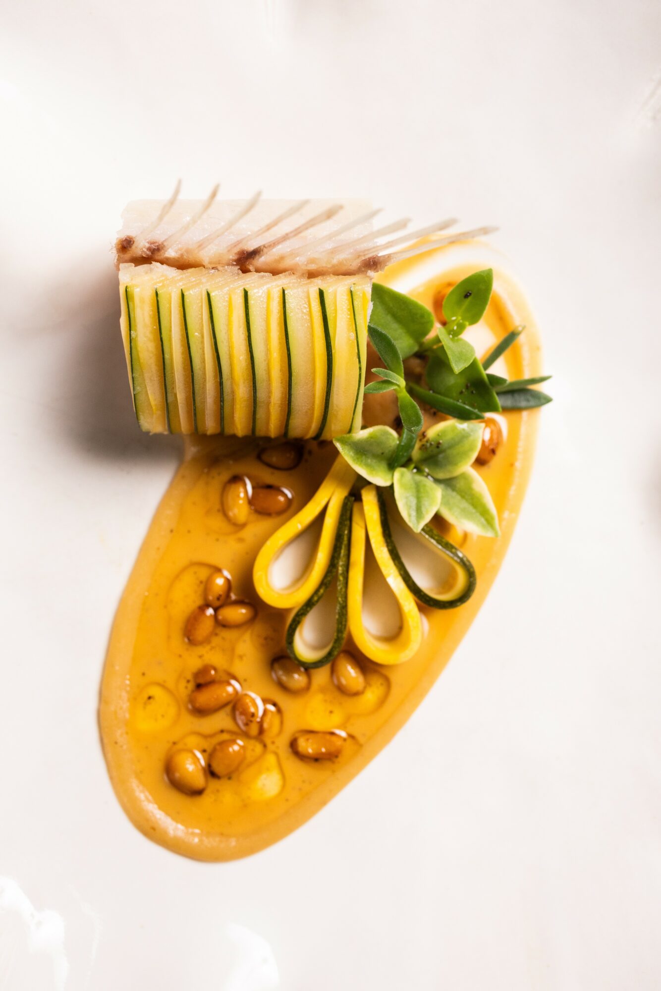 Arrangement of sliced fruits and a yellow sauce with seeds on a white surface.