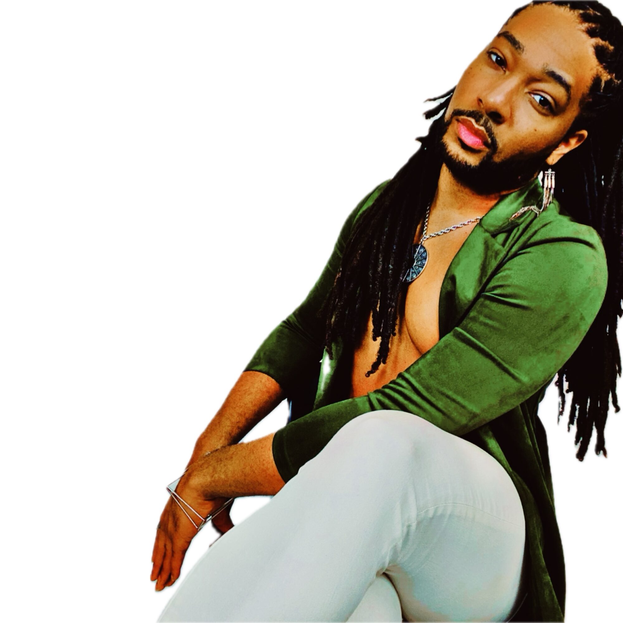 Person with long dreadlocks, wearing a green jacket and white pants, sitting and looking at the camera.