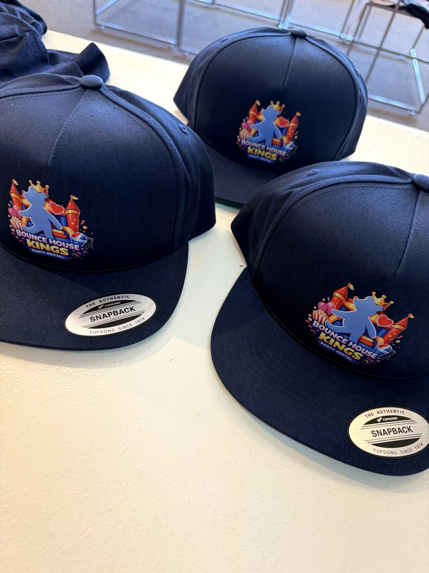Three navy blue snapback hats with a colorful logo of a ship and crown, placed on a white surface.