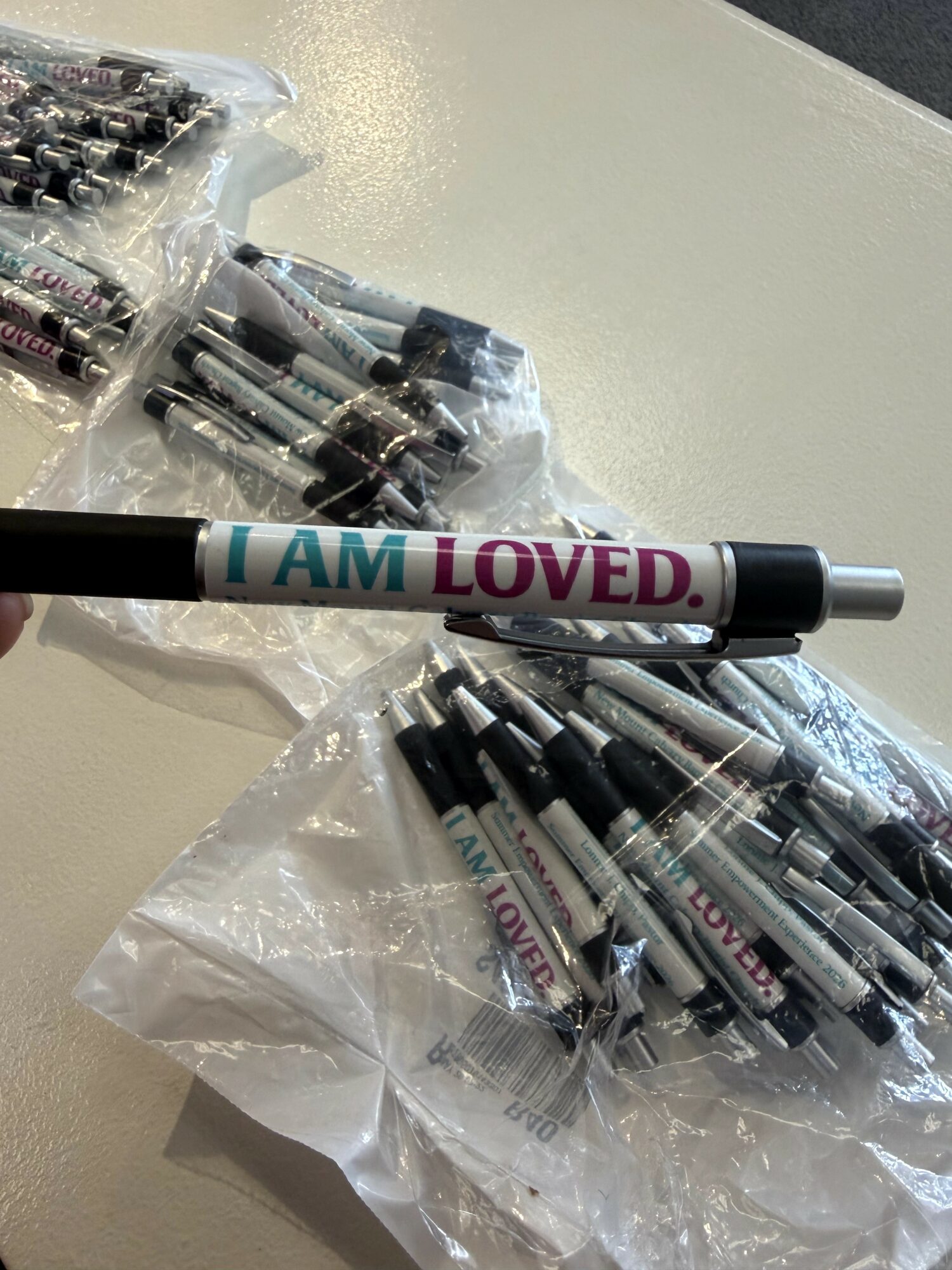 Marker with text 'I AM LOVED' lying on a table with plastic bags of markers nearby.
