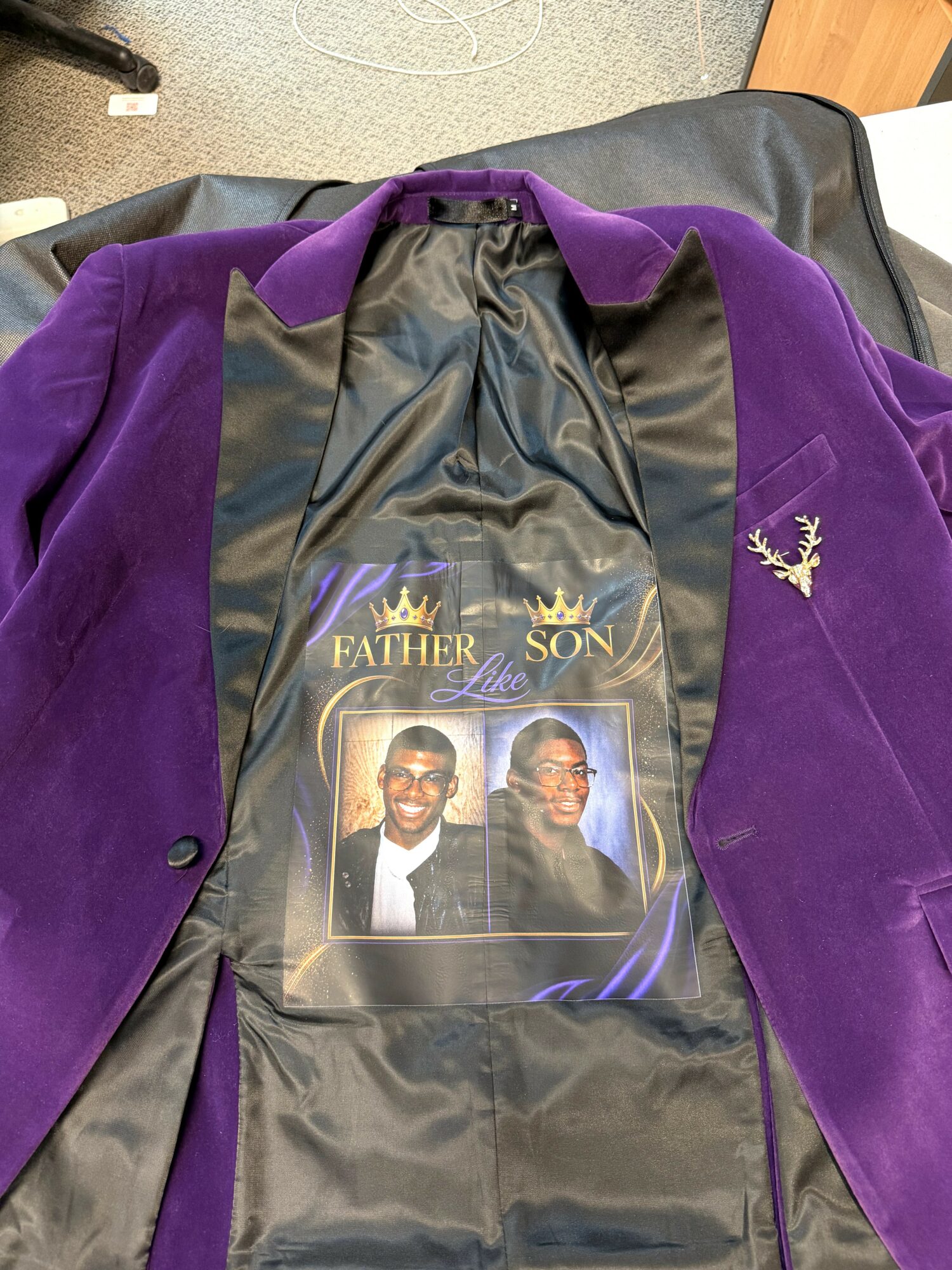 Purple blazer with a photo of two men, one with glasses, and a gold crown logo inside, on a black lining.
