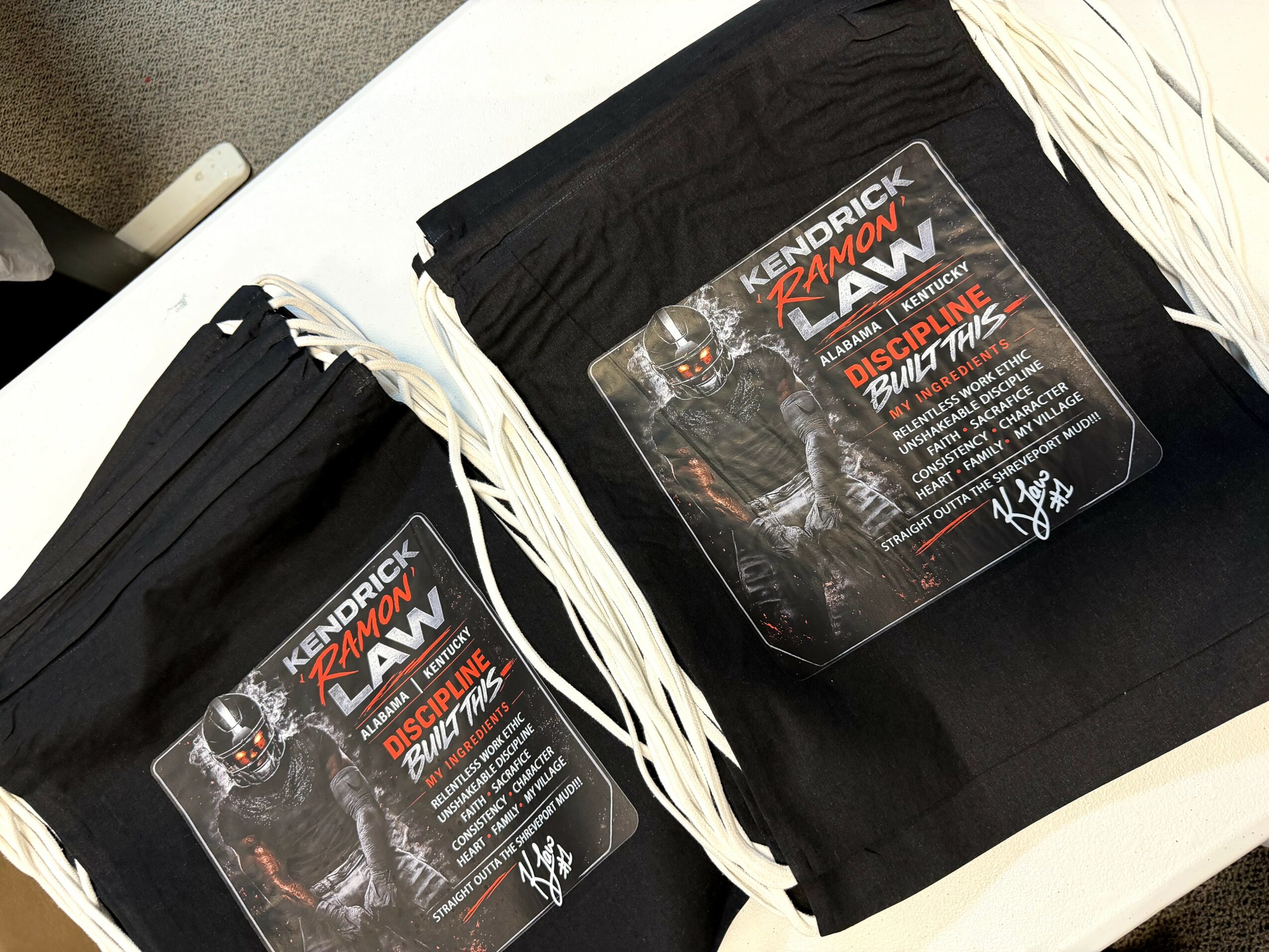 Two black drawstring bags with wrestling event posters on a white surface.
