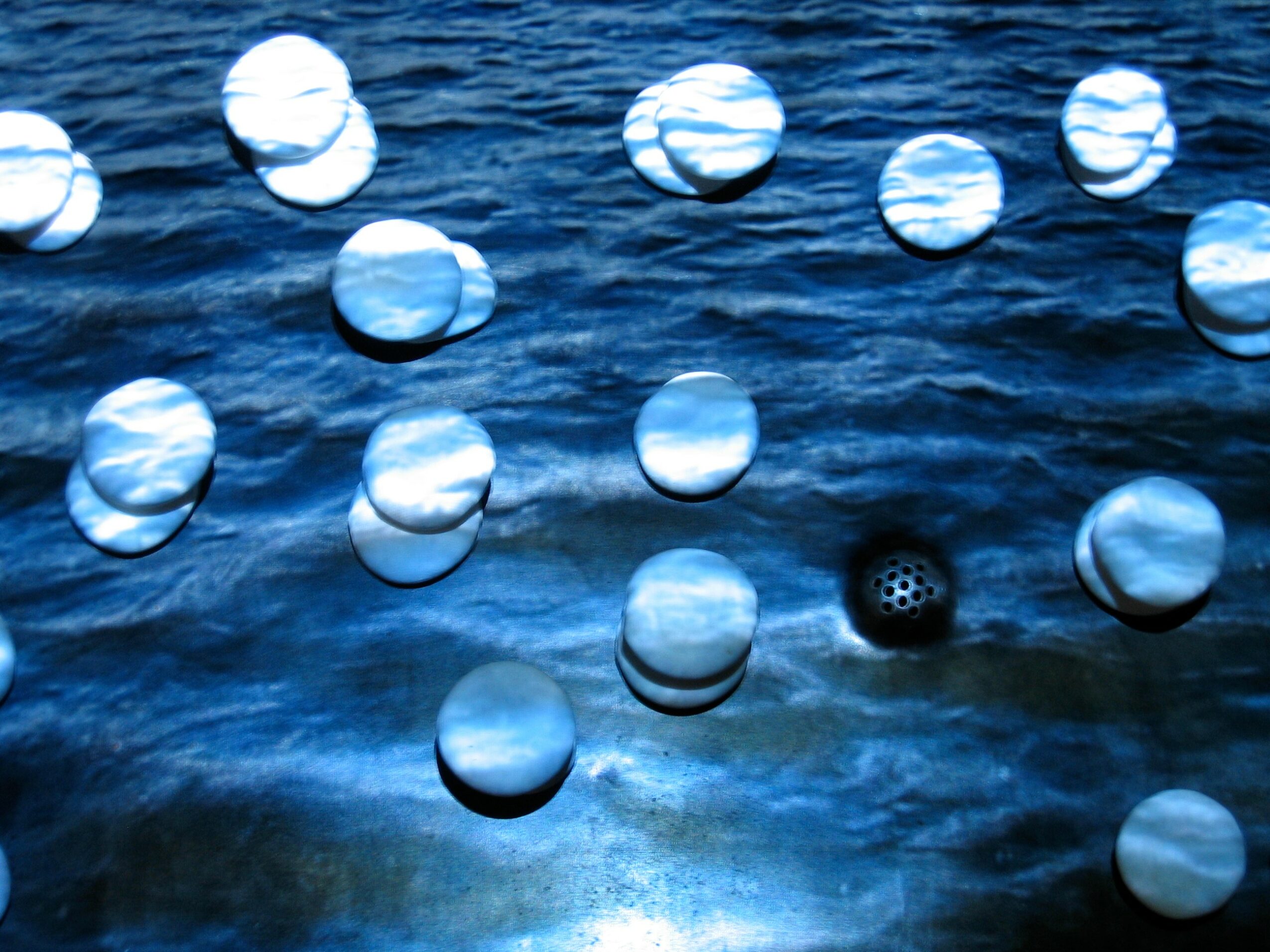 Multiple reflective spheres floating on water surface, some with ripples, with one black sphere among them.