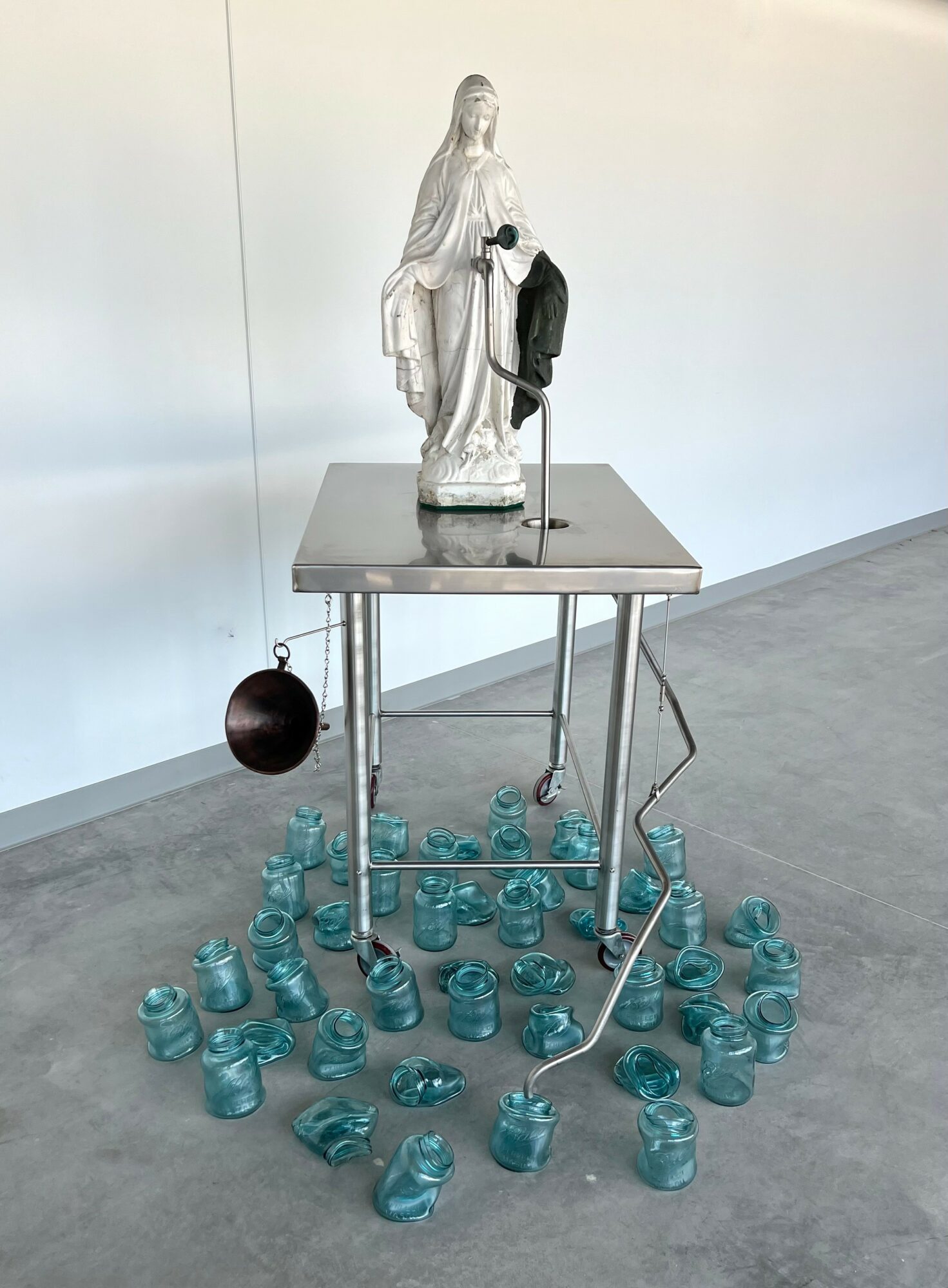 Statue of a woman with a black bag on a table, surrounded by blue glass jars on the floor.