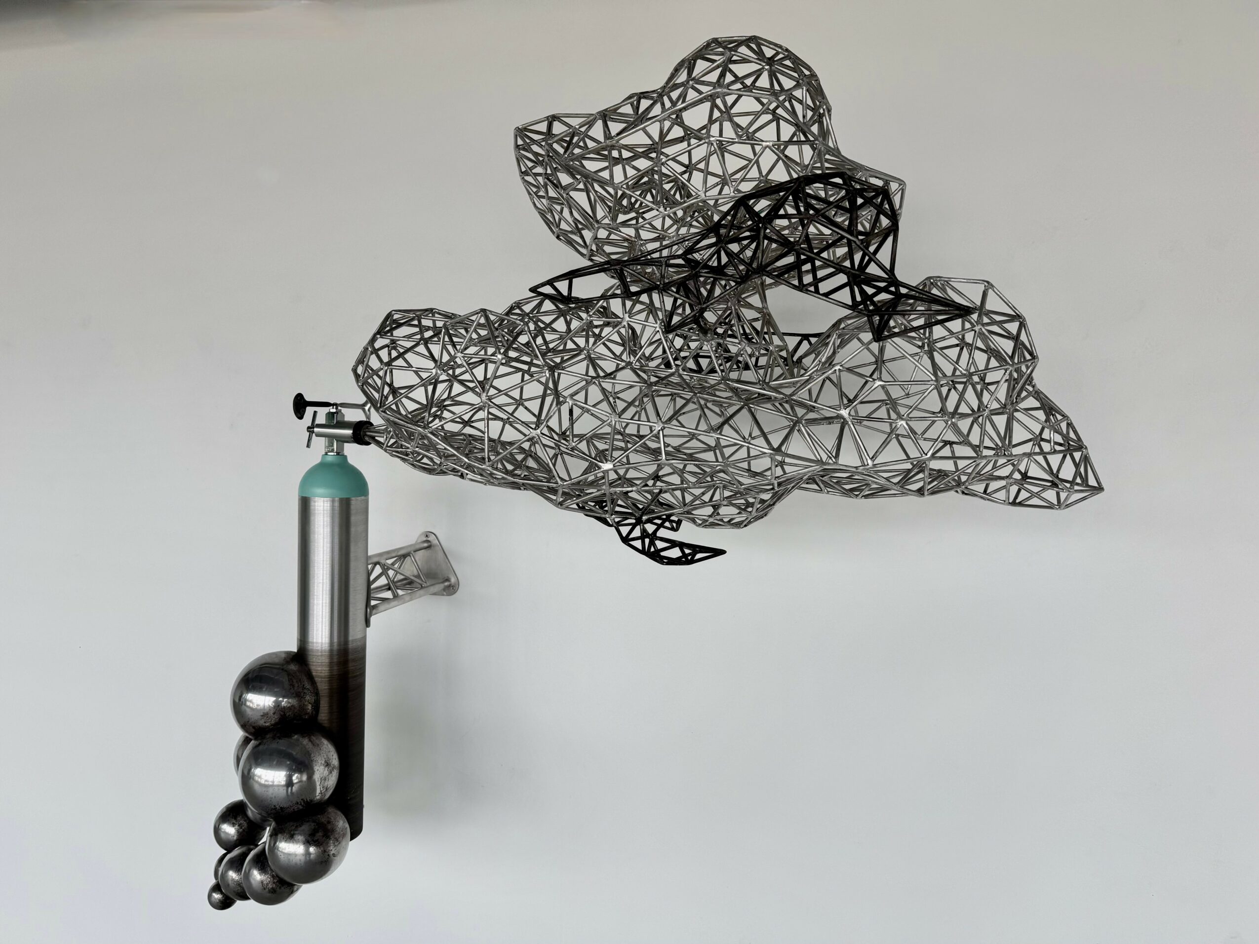 Metal sculpture resembling a cloud with a cluster of metallic spheres attached to a vertical pipe, on a plain background.