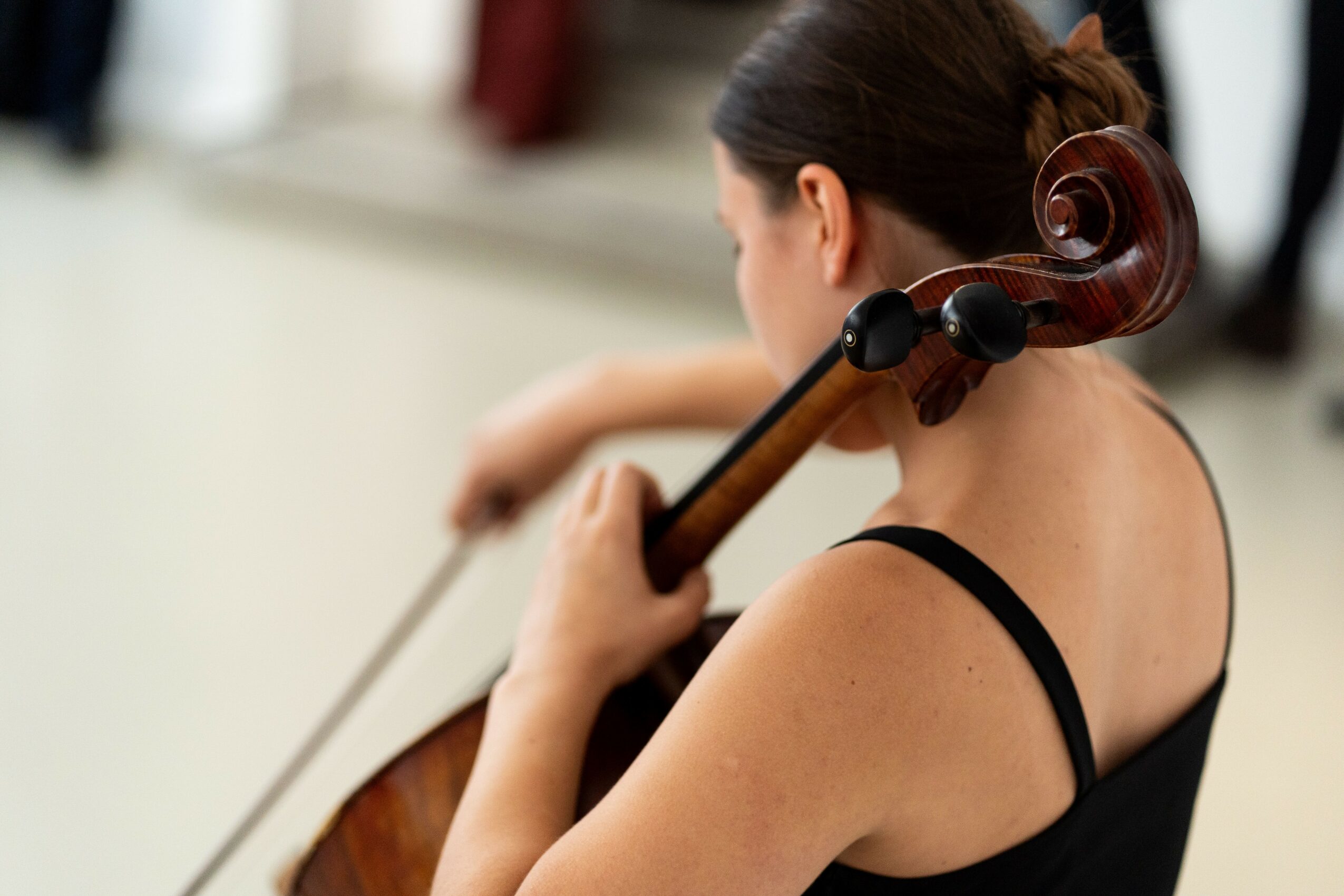 Woman playing a cello, viewed from behind, with a blurred background.