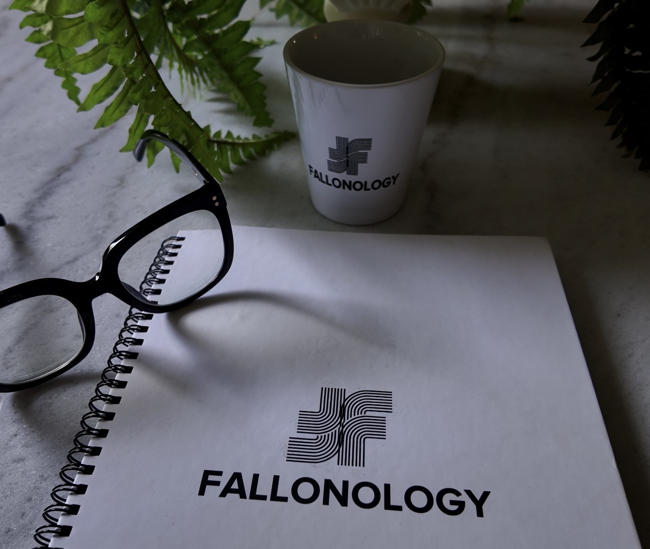 Notebook with logo and text, glasses, plant leaves, and a cup on a surface.