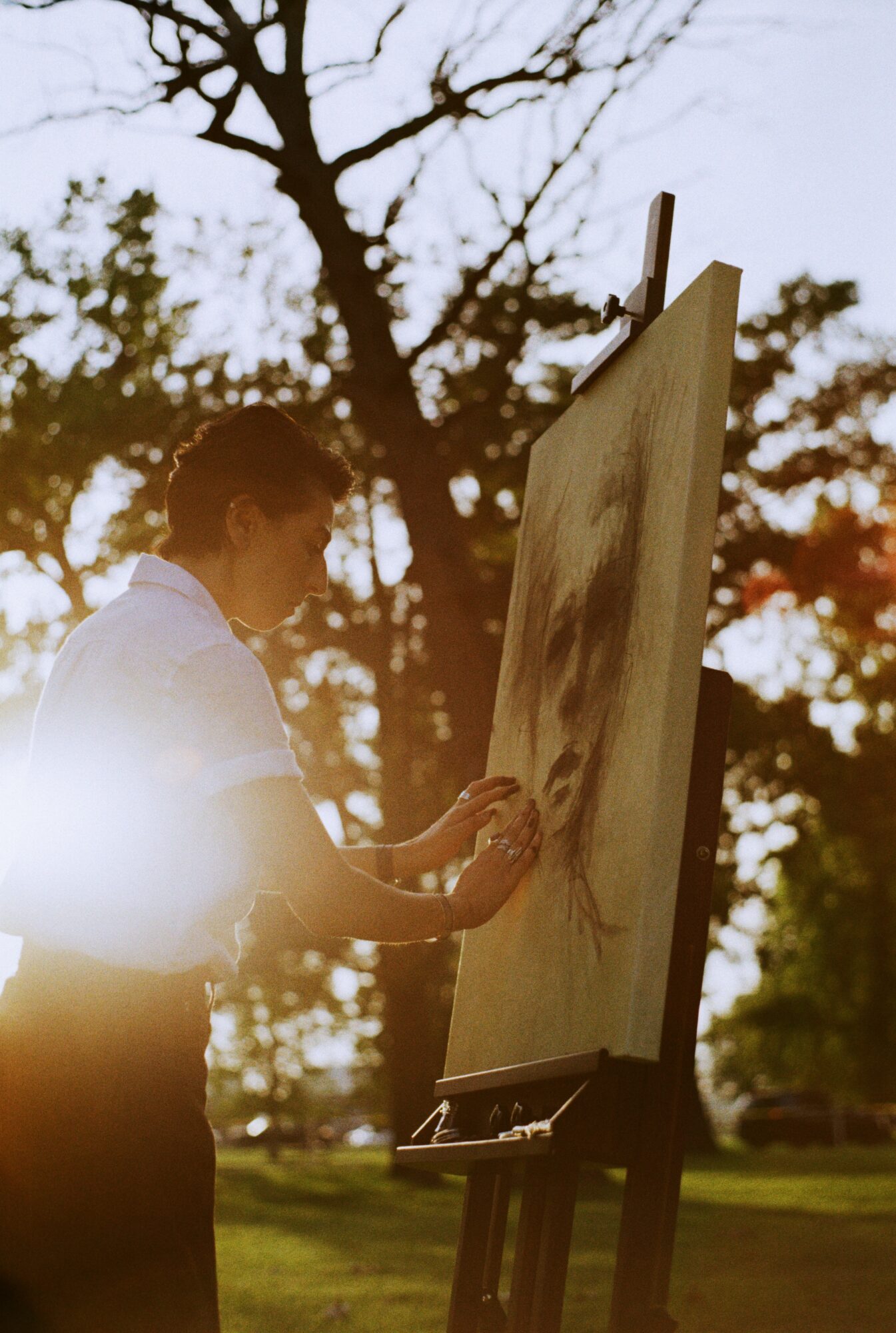 Person painting on an outdoor canvas with trees and sunlight in the background.