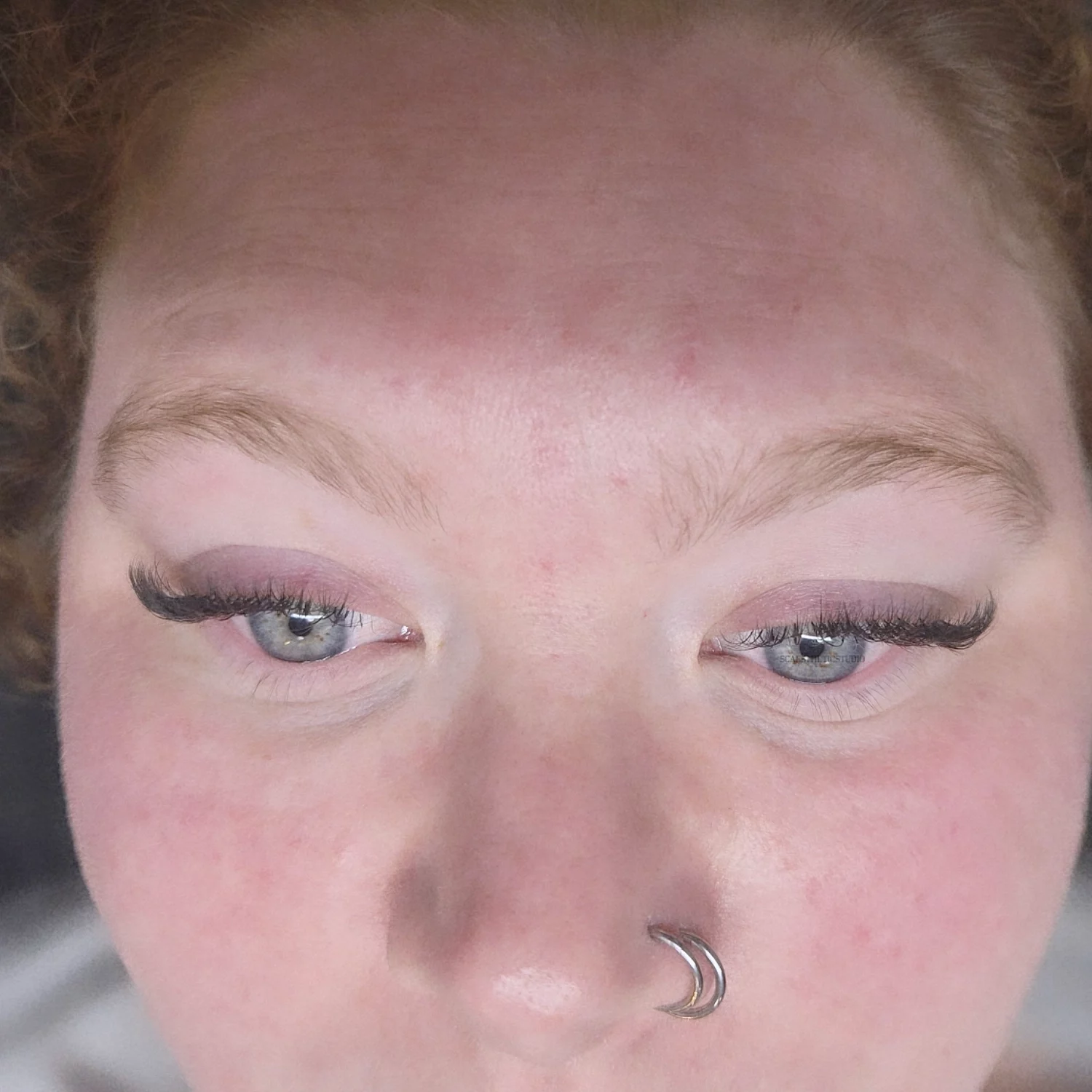 Close-up of a person's face with light skin, blue eyes, and makeup, lying sideways. The face is rotated 90 degrees clockwise.