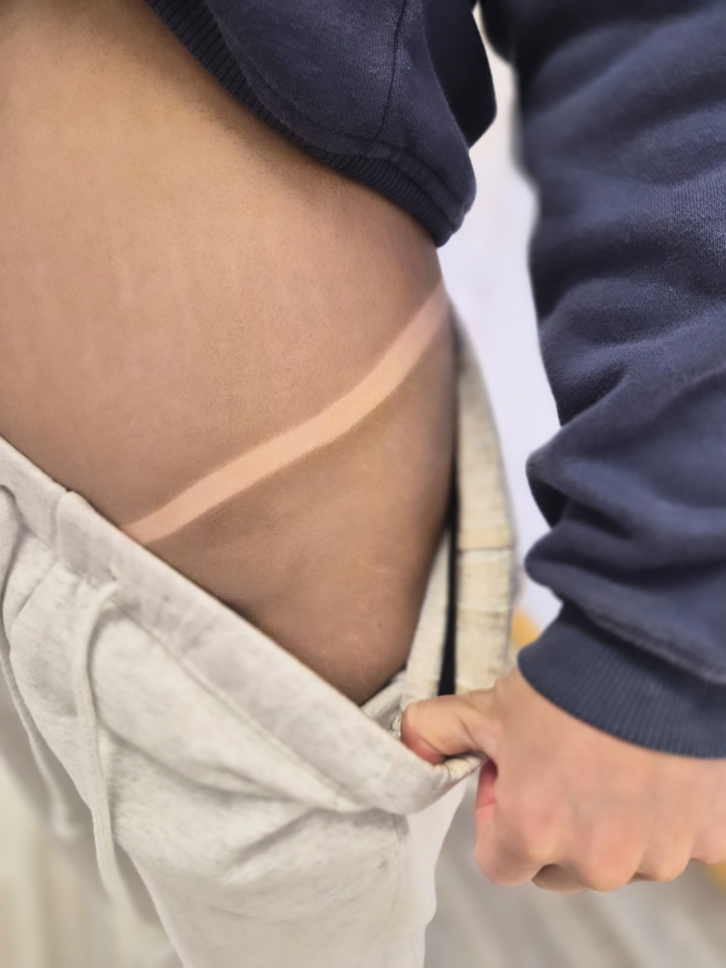 Person wearing a navy jacket and light gray pants, with a visible tan line on the waist.