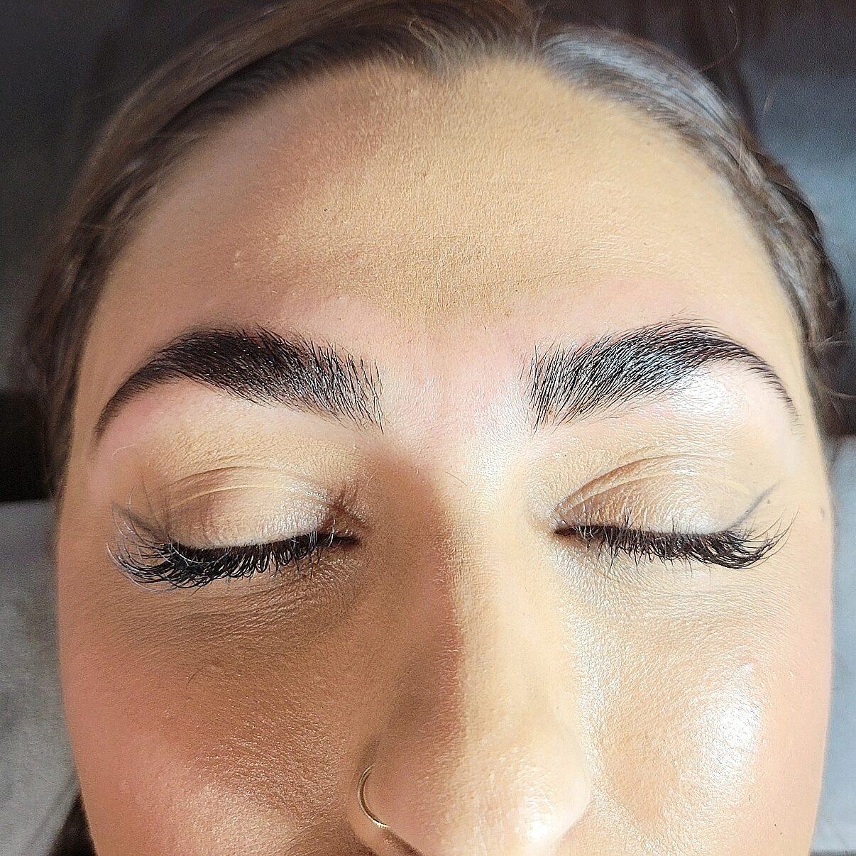 Close-up of a person's face with closed eyes, showing well-groomed eyebrows and smooth skin.