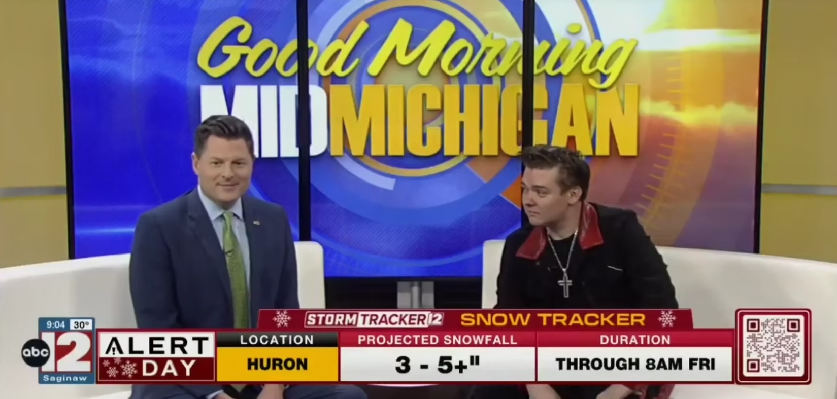 Two men sit at a news desk with a colorful background displaying 'Good Morning Michigan' and weather graphics.