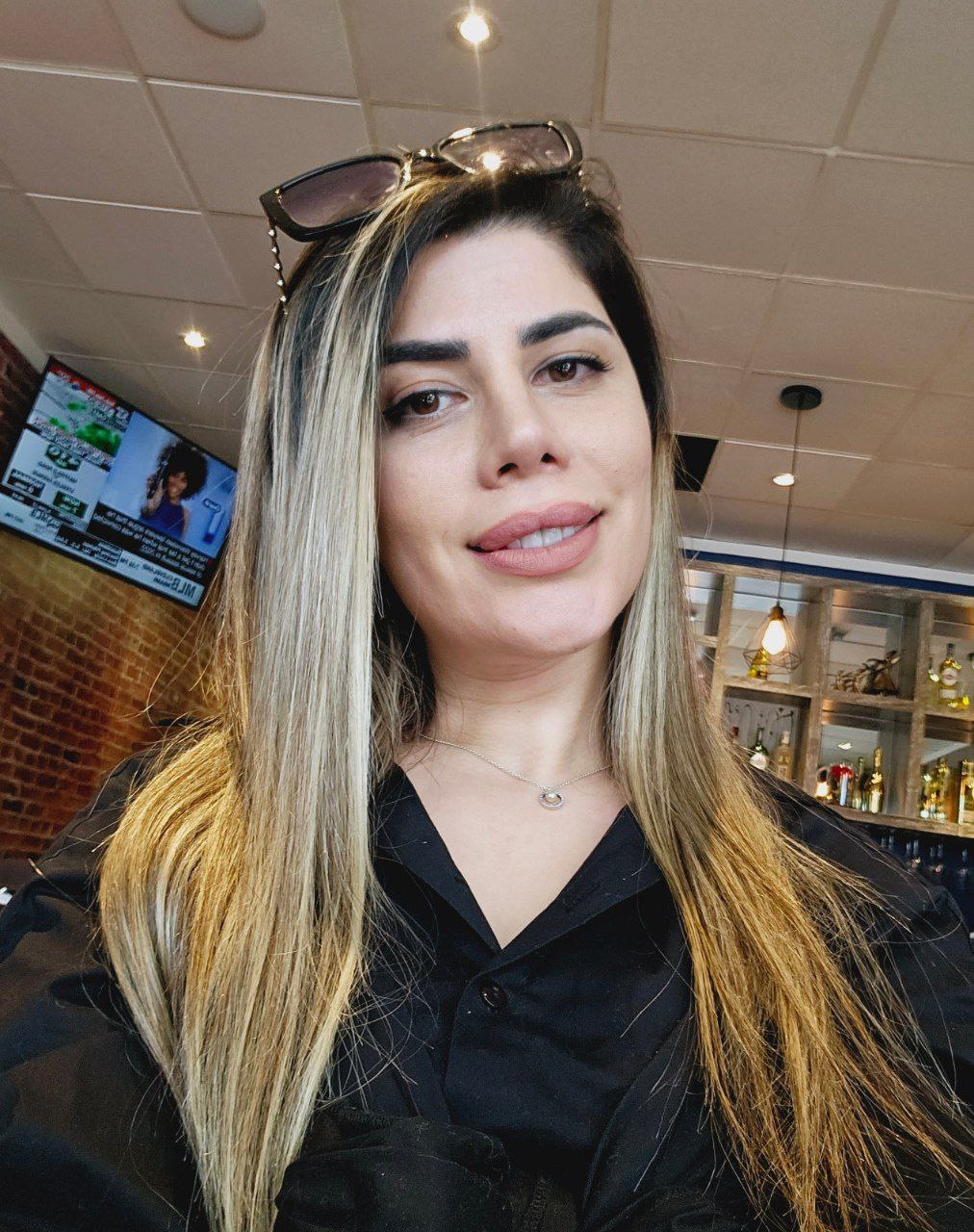 Woman with long hair and sunglasses on her head, smiling in a cafe or bar setting.
