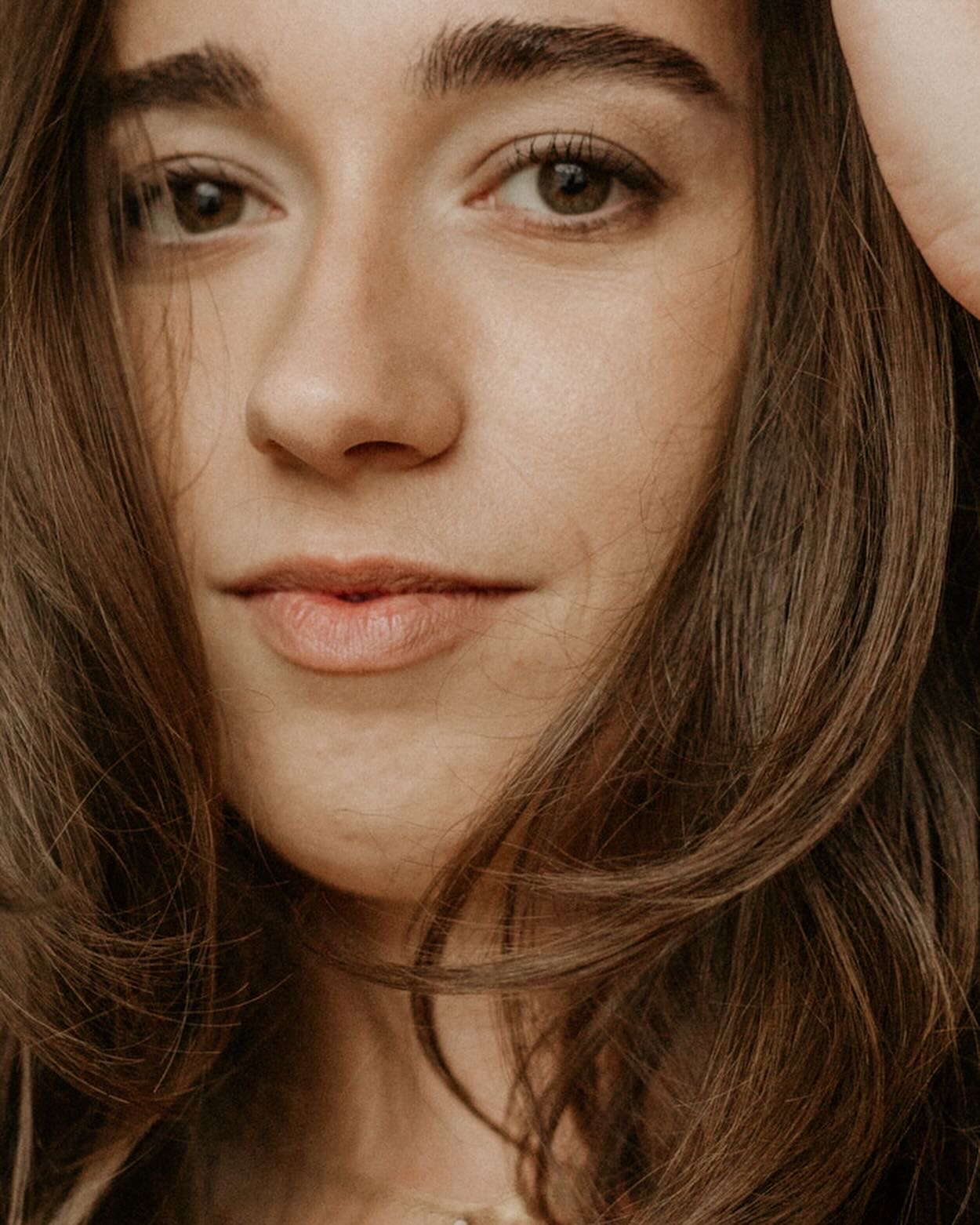 Close-up of a young woman with long brown hair, neutral expression, and light makeup.
