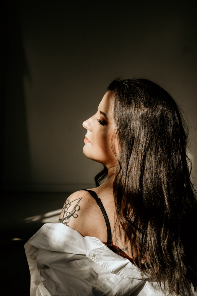 Side profile of a woman with long dark hair, wearing a black strap top and white shirt, looking to the left.