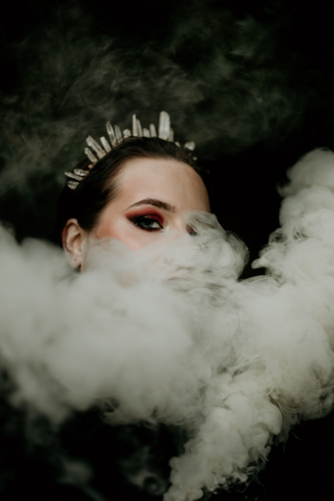 Partially visible woman's face with makeup, surrounded by smoke and dark background.