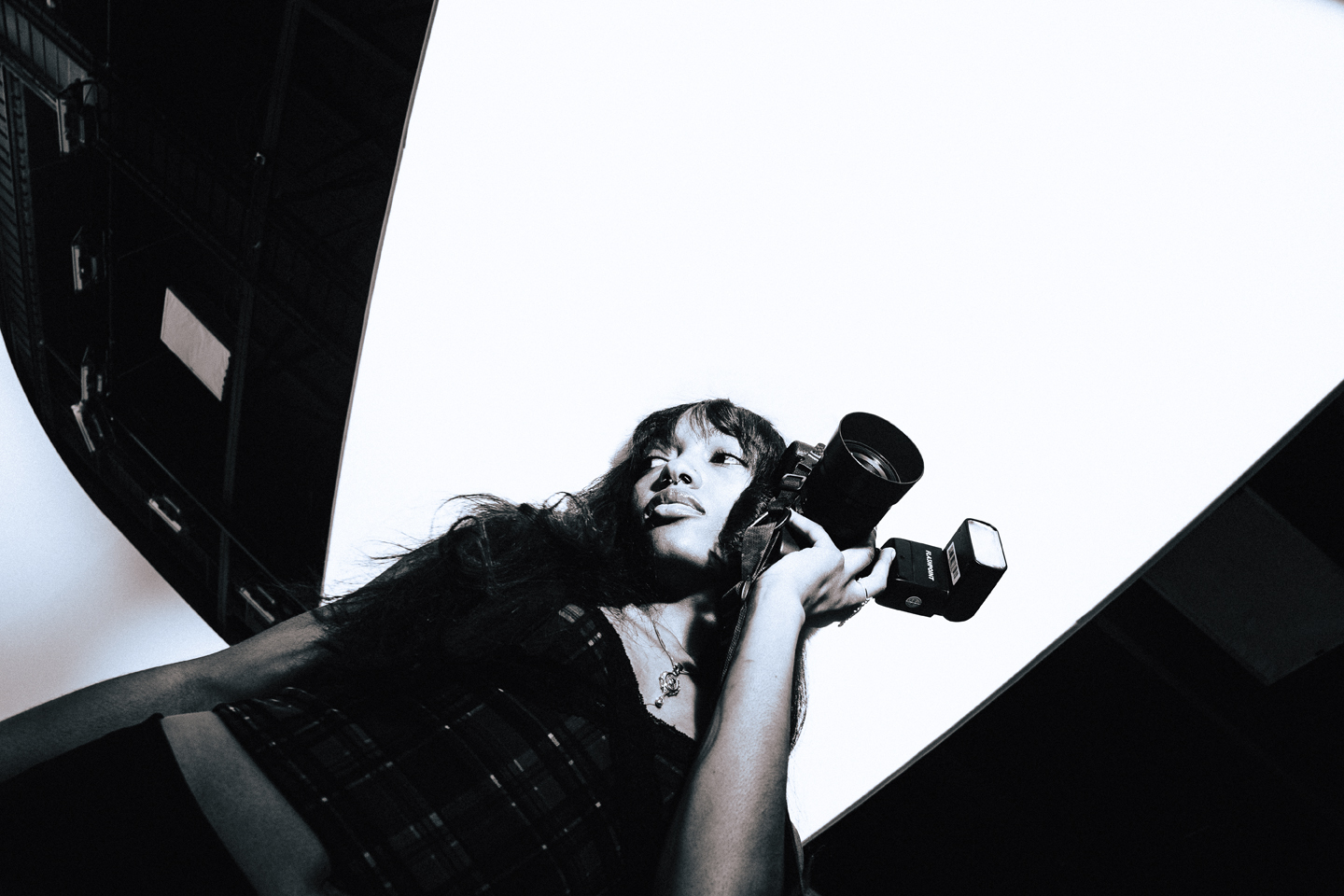 Woman holding a camera, looking upward, with a bright light background, in black and white.