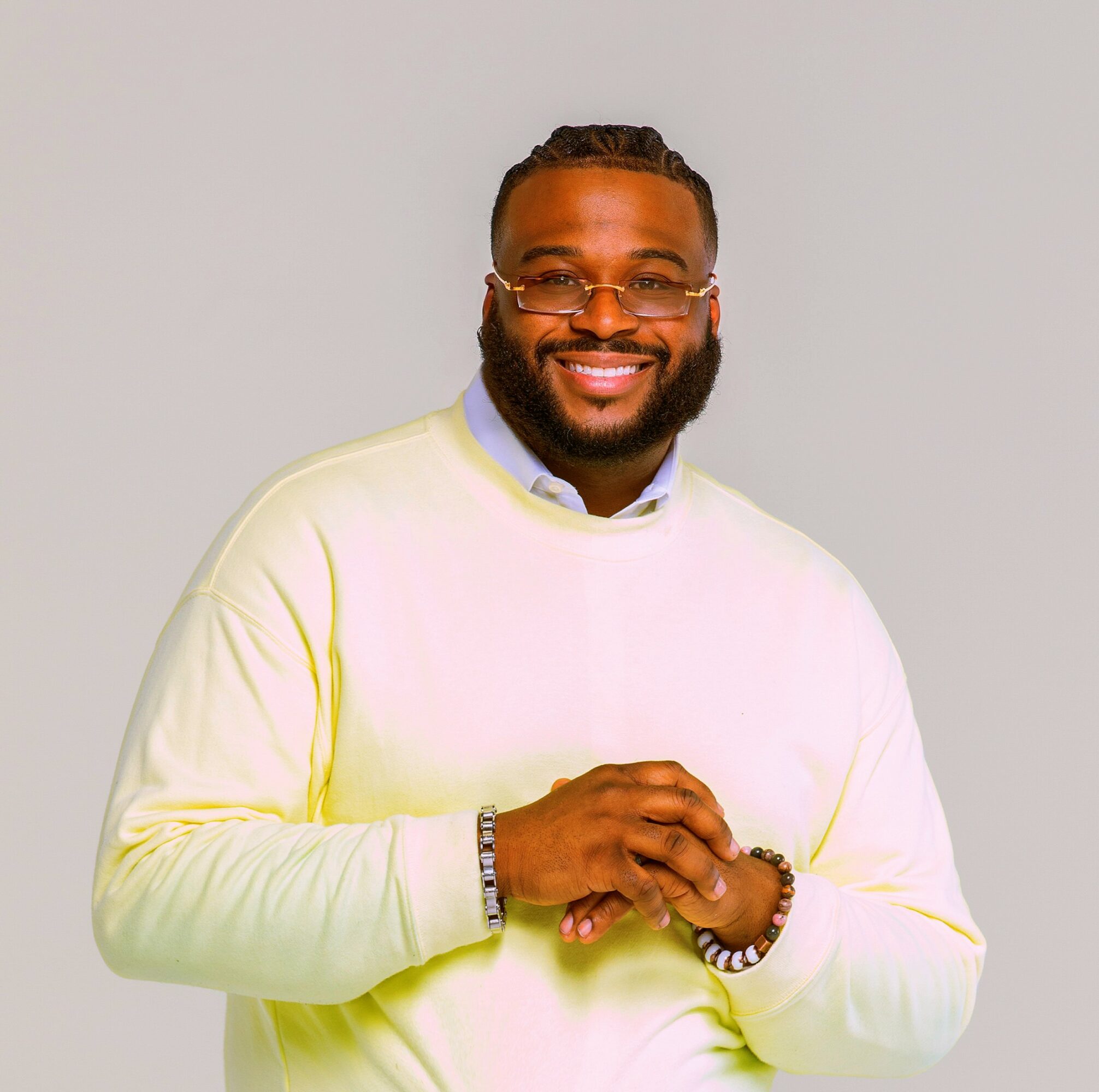 Smiling man with glasses and a beard, wearing a light-colored sweater, standing against a plain background.